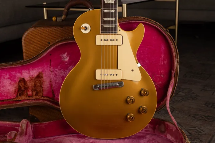 A 1954 Gibson Les Paul Goldtop with cream P-90 pickups and a cream pickguard, resting upright in its original brown hardshell case with worn pink lining.