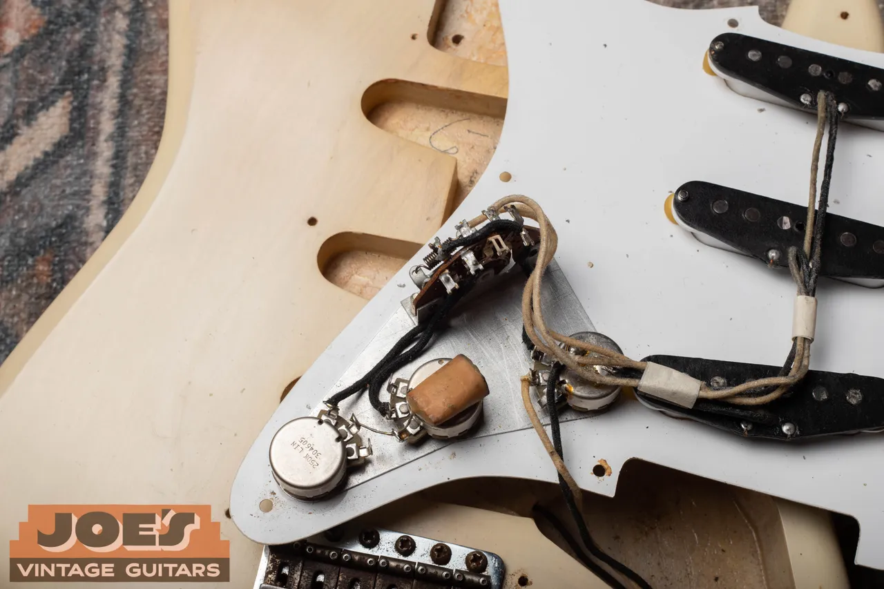 The square wax-dipped phone book capacitor sitting on the tone pot of a 1956 blonde Fender Stratocaster, next to a pot stamped 250K LIN 304605