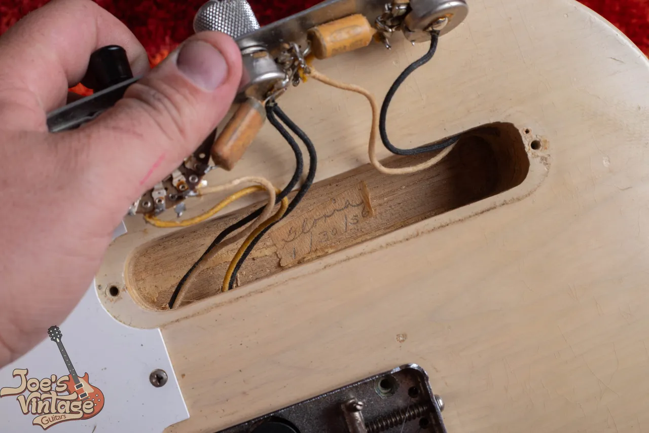 A strip of masking tape inside the control cavity of a 1956 Fender Telecaster, handwritten with a worker's name and the date