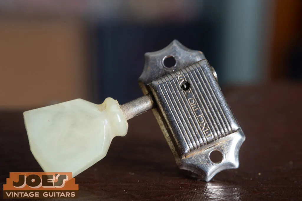 Close-up of a 1956 Gibson Les Paul Kluson Deluxe “Single Line” tuner housing, showing the “Kluson Deluxe” stamp and an aged cream tulip button.