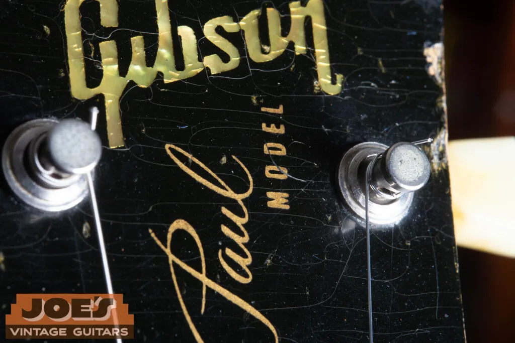 Close-up of a 1956 Gibson Les Paul headstock featuring the Mother of Pearl Gibson inlay and the gold “Les Paul Model” silkscreen, showing the specific mid-50s font and the vertical spacing between the logo and the script.