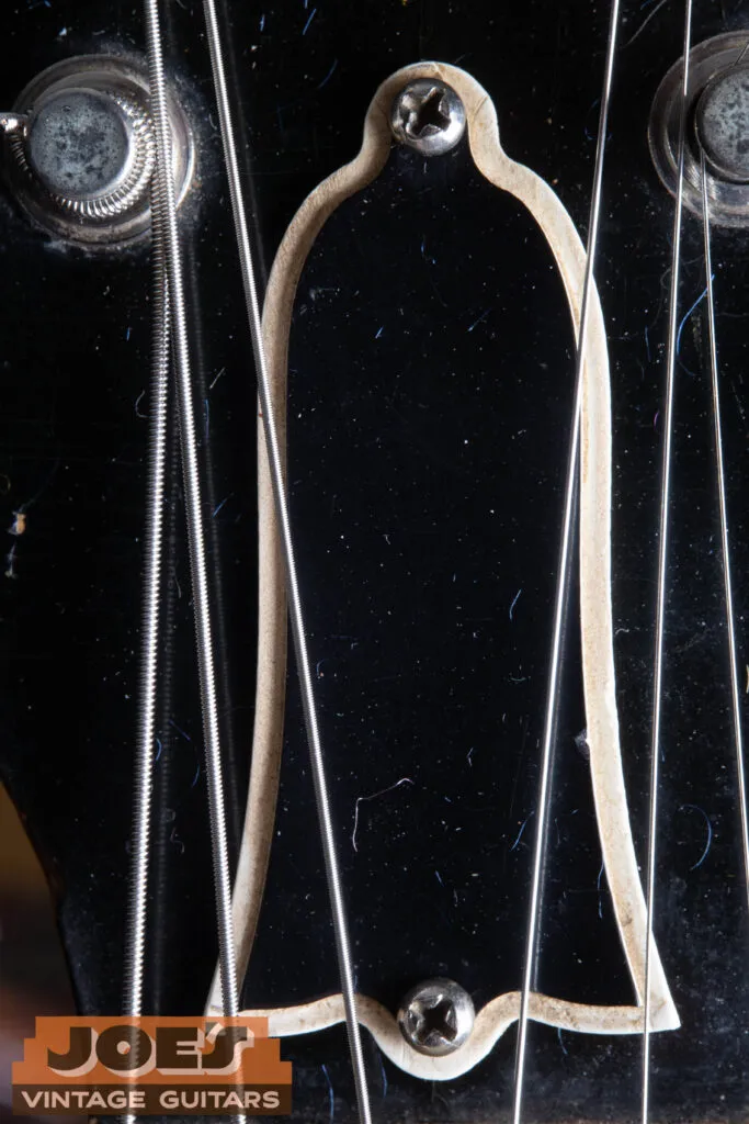 Macro close-up of a 1956 Gibson Les Paul truss rod cover, showing the period-correct two-ply black and white bell-shaped plastic and the original mounting screws.