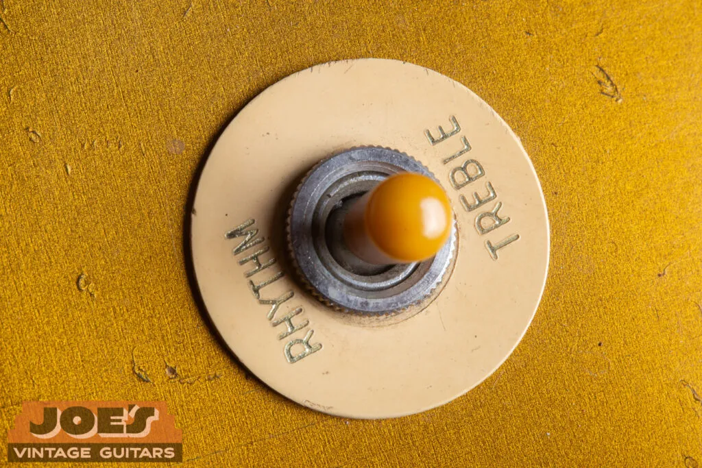 Close-up of a 1956 Gibson Les Paul 3-way toggle switch featuring an aged amber Catalin tip and a cream “poker chip” selector ring with gold-embossed lettering.