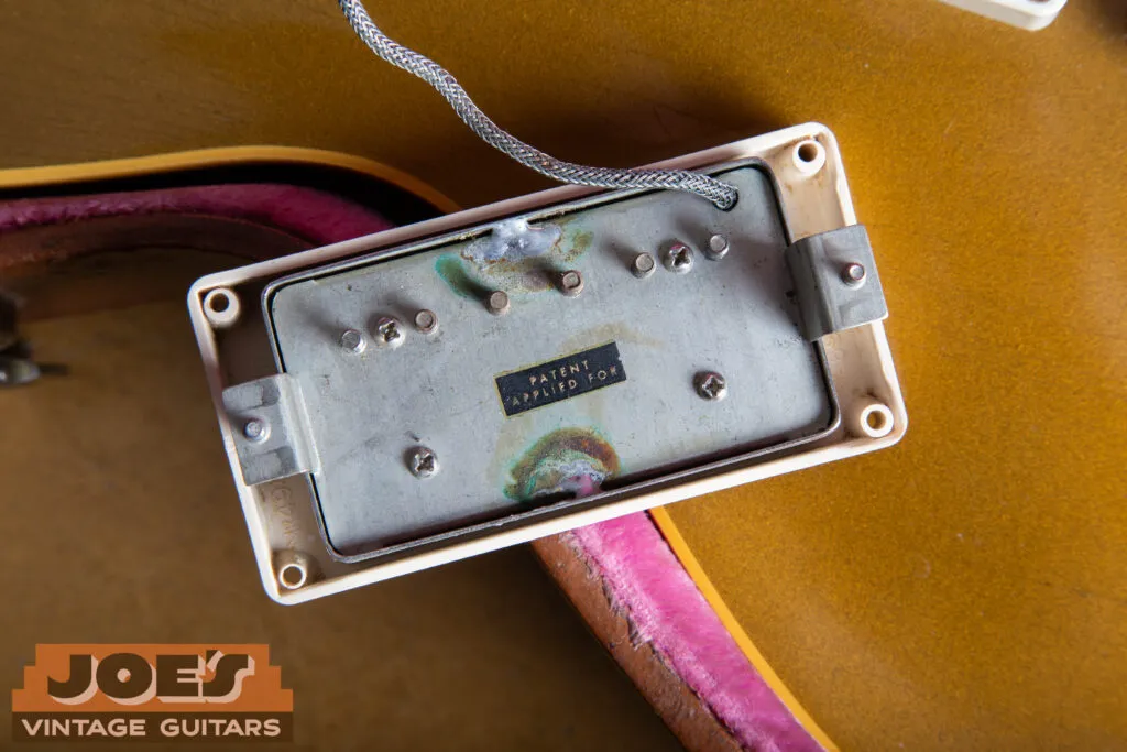 Macro close-up of the underside of a 1957 Gibson PAF humbucker, showing the original patent applied for decal, black “L” tool marks on the square mounting feet, and “M-69” stamps inside the cream pickup ring.