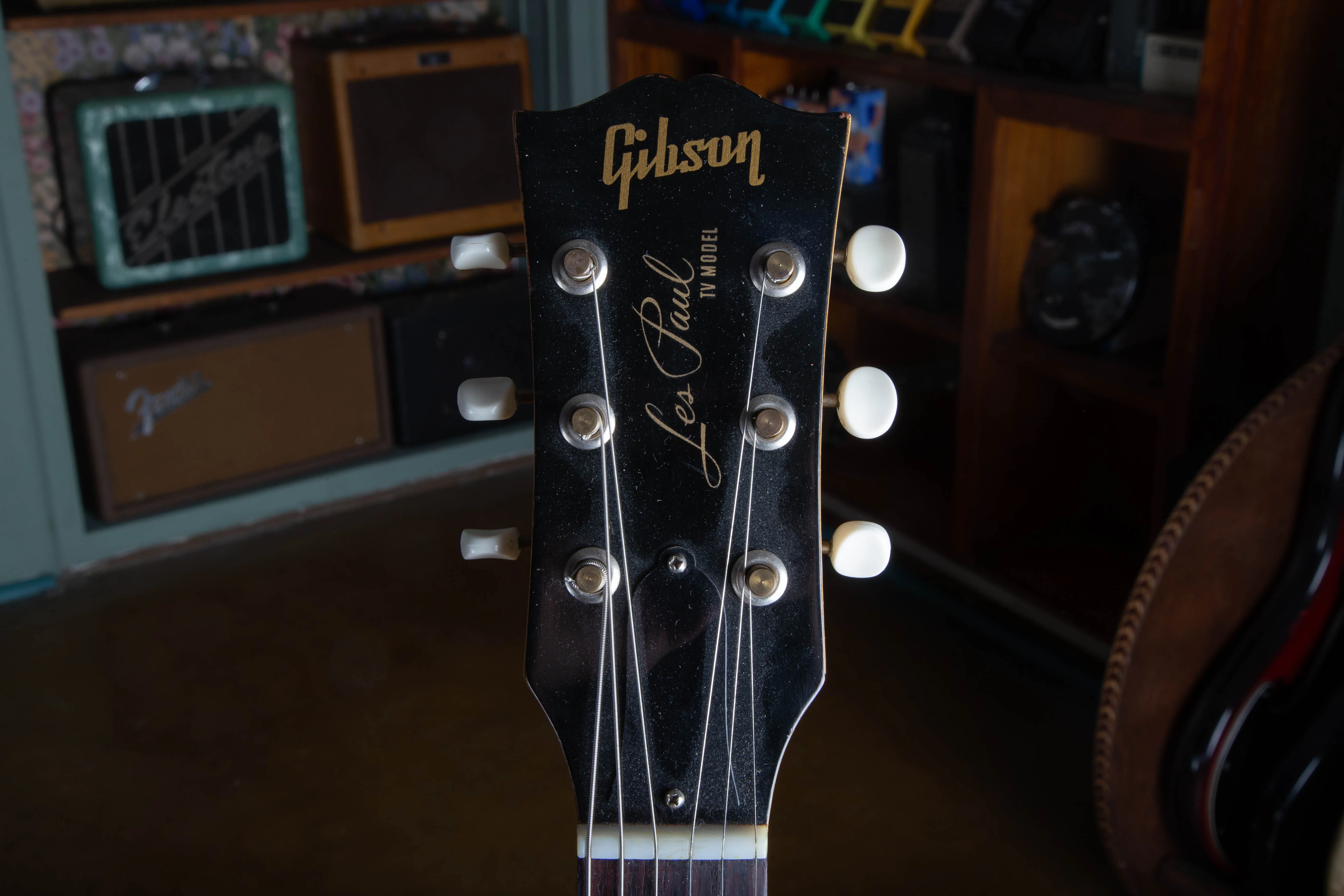 Front of the headstock of a 1957 Gibson Les Paul TV Model, showing the black headstock face with the gold Gibson logo and Les Paul TV Model silk-screen, and the three-on-a-strip Kluson Deluxe tuners with cream plastic buttons.