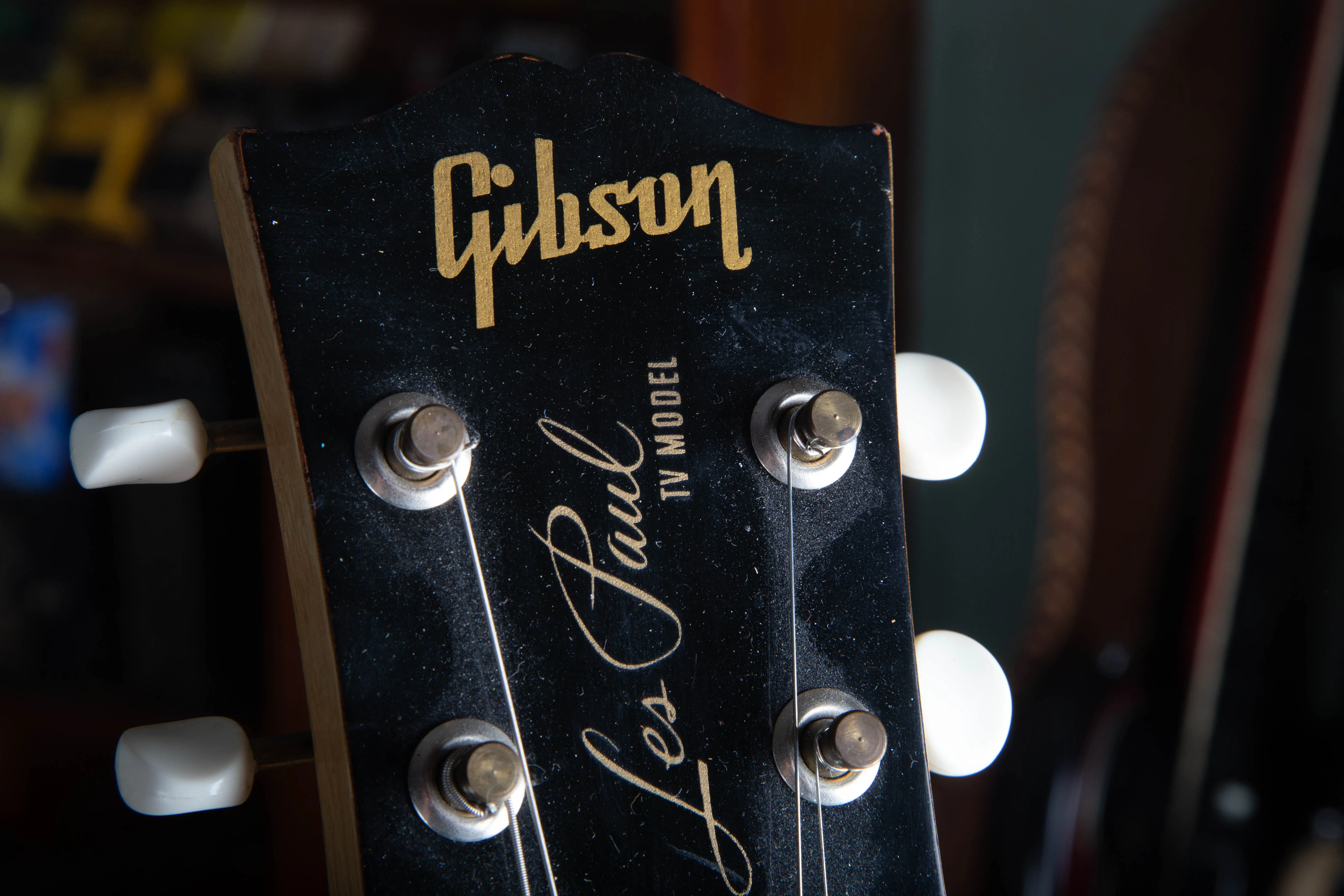 Extreme close-up of the headstock silk-screen on a 1957 Gibson Les Paul TV Model, showing the gold Gibson logo, the Les Paul signature script, and the words TV MODEL in small gold capital letters on the aged black headstock face.