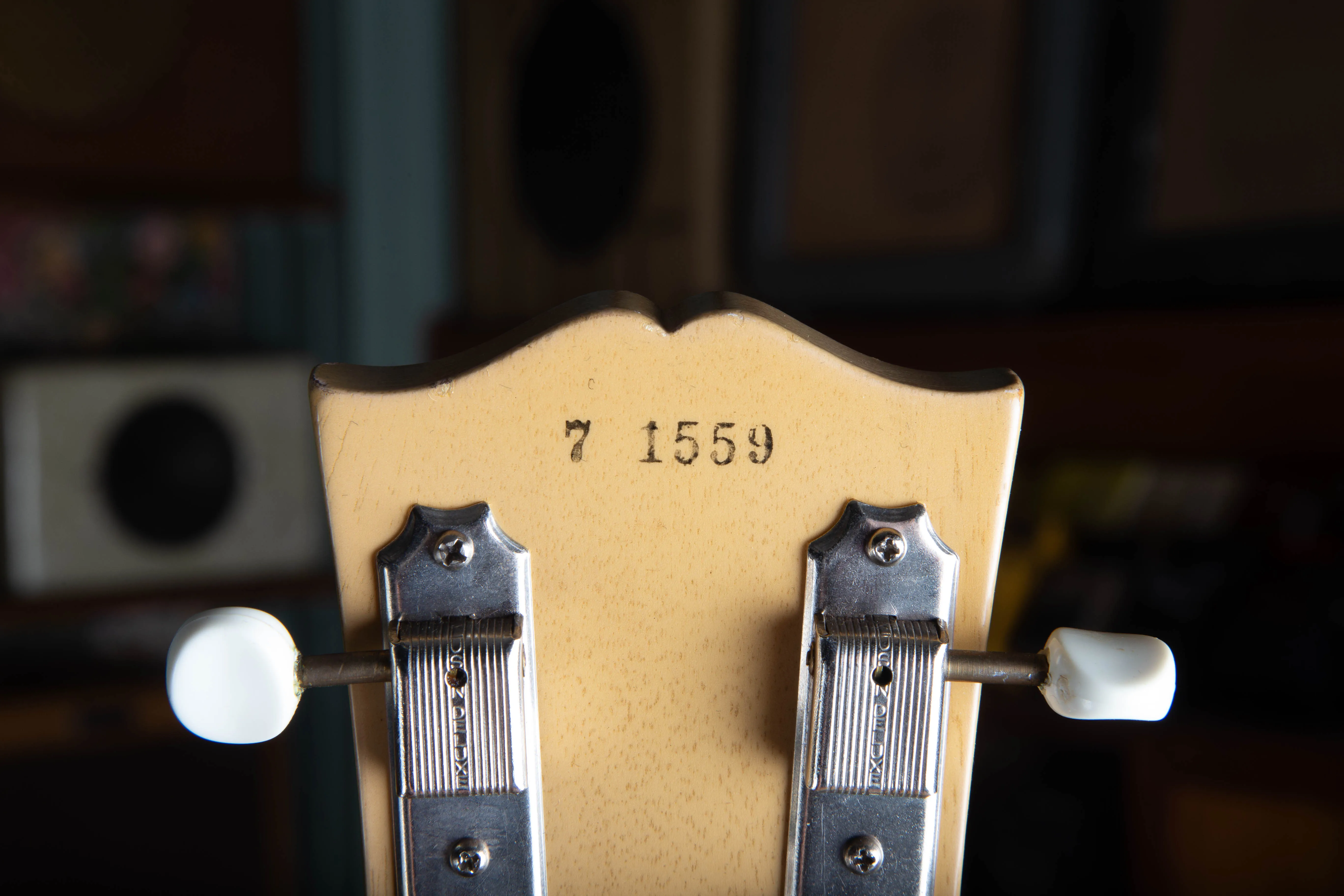 Close-up of the back of the headstock of a 1957 Gibson Les Paul TV Model, showing the black ink-stamped serial number 7 1559 on the limed mahogany finish, above the Kluson Deluxe strip tuners with their aged brass posts and plastic buttons.
