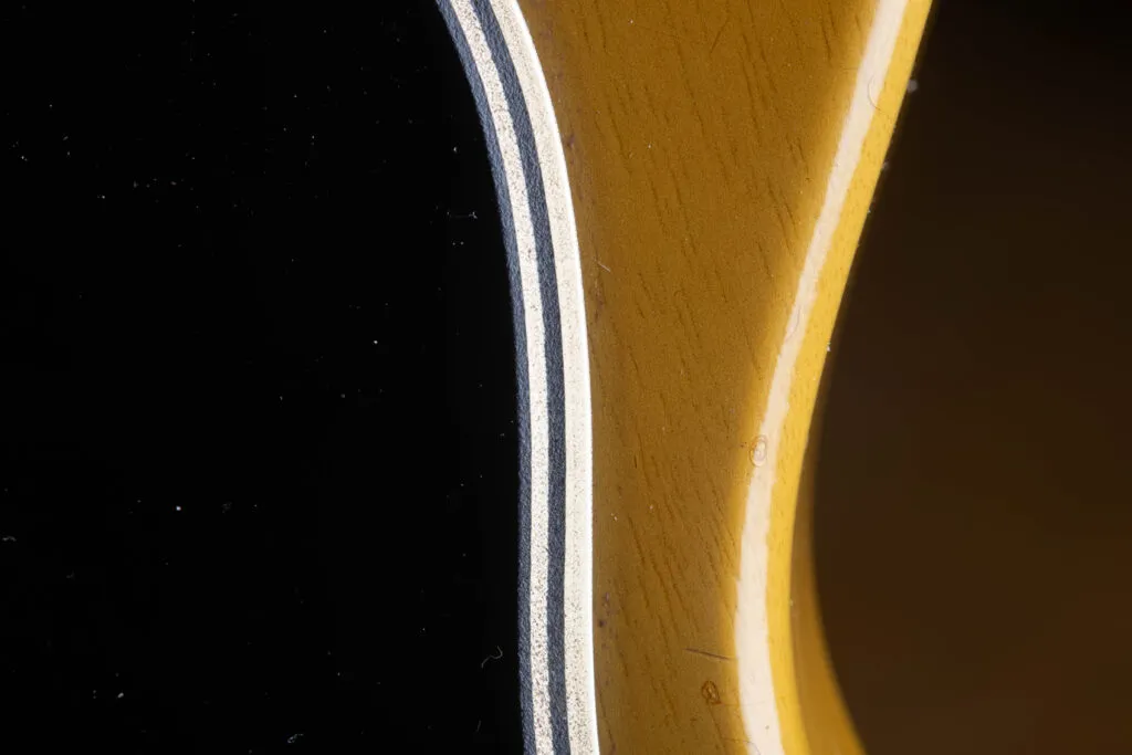 Side-angle perspective of an original 1957 Gibson Les Paul Special pickguard, showcasing the distinct 5-ply laminate construction. The edge clearly displays the alternating layers of Black/White/Black/White/Black plastic, with visible signs of natural aging, slight beveling from the factory, and minor surface scratches characteristic of “Golden Era” use.