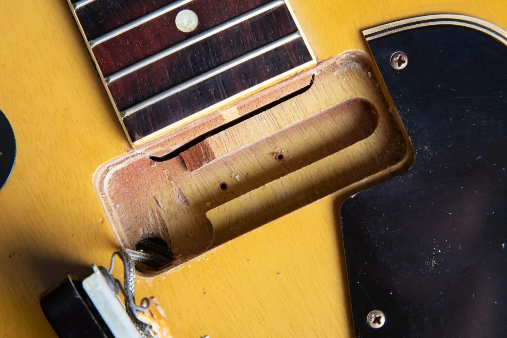 Top-down macro view of a 1957 Gibson Les Paul Special neck pickup routing. The image highlights the distinctive slim channel at the base of the cavity and the exposed end of the mahogany neck tenon. Detailed features include the original “Golden Era” mahogany wood grain, factory-drilled mounting holes, and the translucent TV Yellow nitrocellulose finish bleeding over the routed edges.