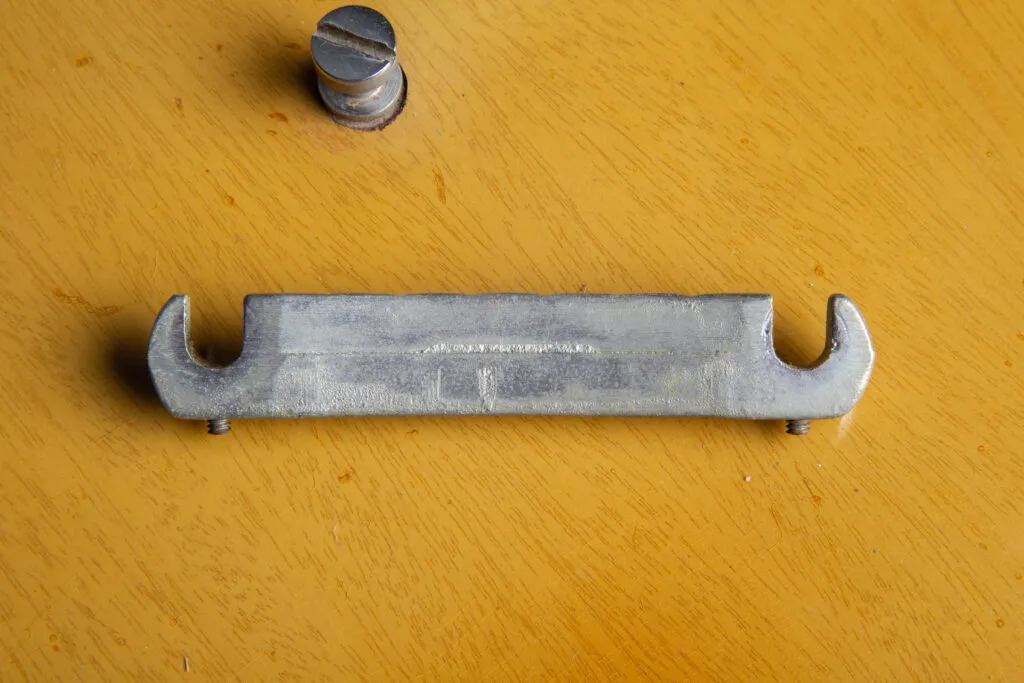 Close-up rear view of an authentic 1957 Gibson Les Paul Special nickel-plated wraparound tailpiece. Detail highlighting the original “short seam” casting line and the two factory-original intonation Allen screws located near the bridge posts. The nickel plating shows natural 1950s patina and oxidation.