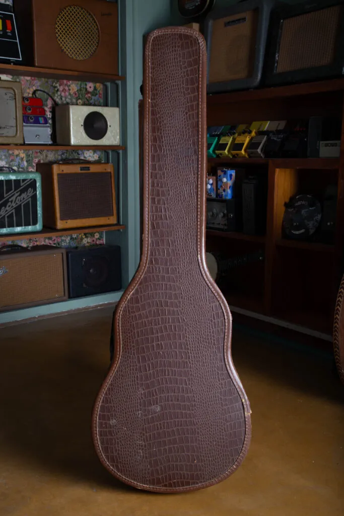 Alt Text A wide perspective of an original 1950s Gibson “alligator” chipboard guitar case. The image highlights the distinctive textured exterior that mimics the look of alligator skin, along with the vintage-style plastic handle, metal latches, and the characteristic slim, tapered silhouette designed specifically for the 1955 to 1958 Les Paul Special body style.