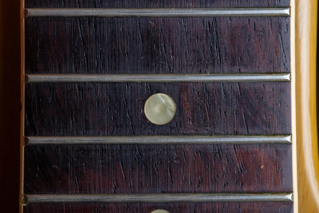 A detailed perspective of an original 1958 Gibson Les Paul Special fretboard dot inlay. The image captures the organic, “wavy” texture of the mother-of-pearl material, showcasing a distinct iridescent shimmer and subtle greenish-grey tinting caused by decades of natural aging on the dark rosewood fingerboard.