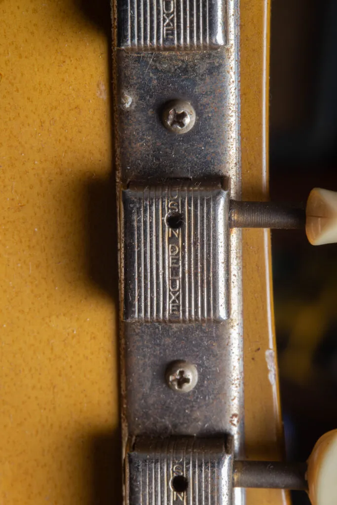 Macro view of the back of 1958 Gibson Les Paul Special headstock featuring original nickel-plated Kluson Deluxe “3-on-a-strip” tuners. The image highlights the “Kluson Deluxe” stamped vertically on each tuner casing and the original plastic buttons. The mahogany wood displays a black ink-stamped serial number and fine nitrocellulose lacquer checking characteristic of “Golden Era” craftsmanship.