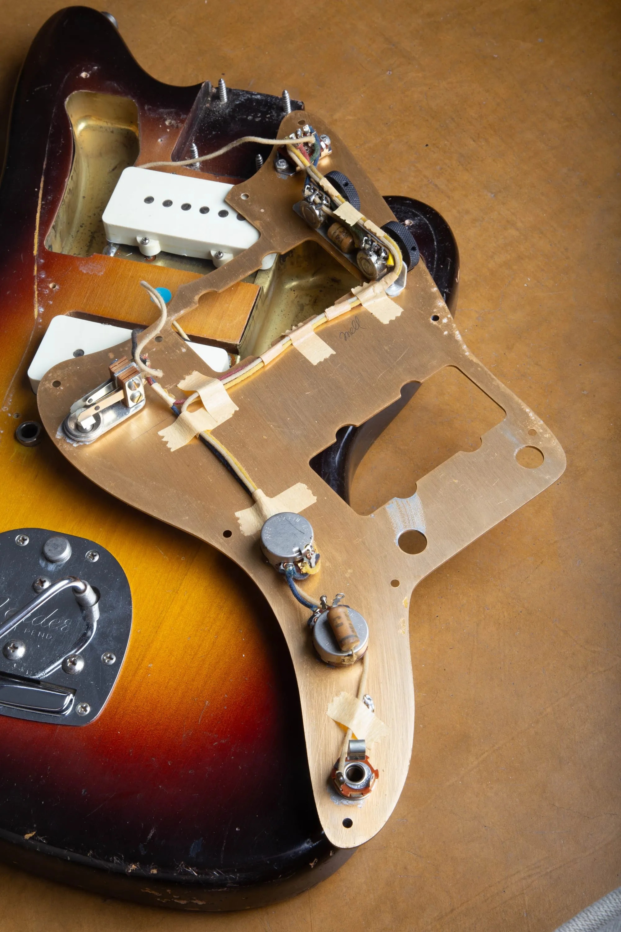 Underside of a 1959 Fender Jazzmaster gold anodized aluminum pickguard lifted from the body, showing the metal shielding plate and the rhythm circuit assembly with cloth wiring