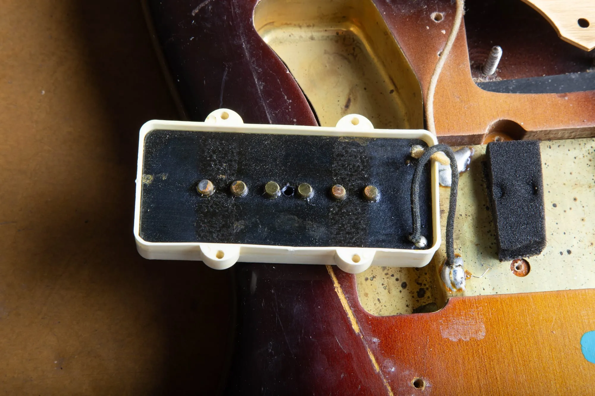 Underside of a 1959 Fender Jazzmaster neck pickup showing black fiber flatwork with six pole pieces and its cloth lead wire, the pre-CBS bobbin bottom, next to the original height-adjustment foam
