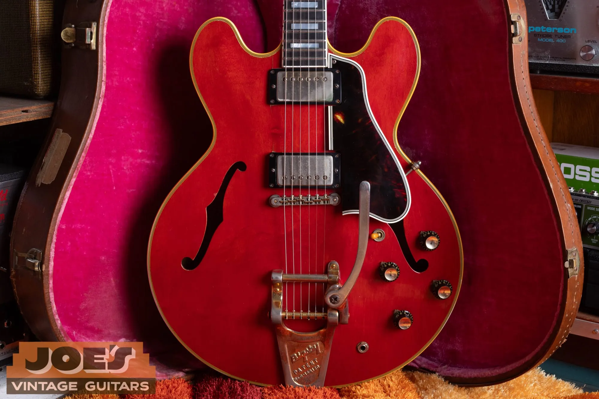 Front of a 1959 Gibson ES-355 in cherry showing the Bigsby vibrato, two gold-cover humbuckers, four knobs, and a bound f-hole, in a pink-lined case.