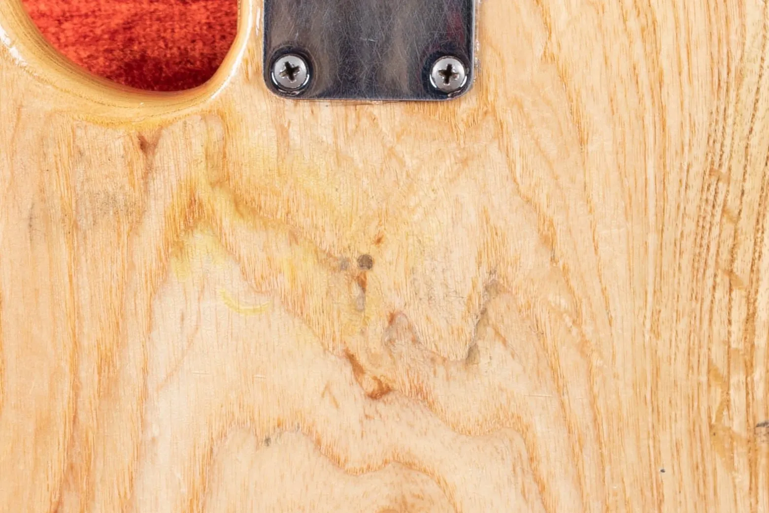 Close-up of the back of a 1960 Fender Precision Bass refinished in natural, showing the small circular pin router template dowel plug in the ash grain below the neck plate.