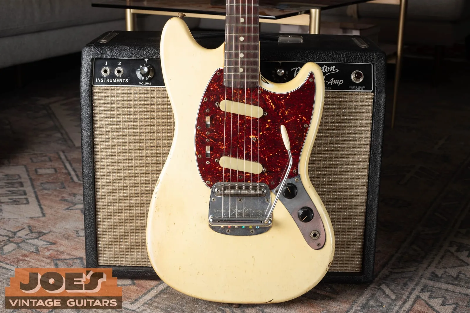 Early 1960s Fender Mustang in Olympic White with a tortoiseshell celluloid pickguard, leaning on a vintage Fender amp.