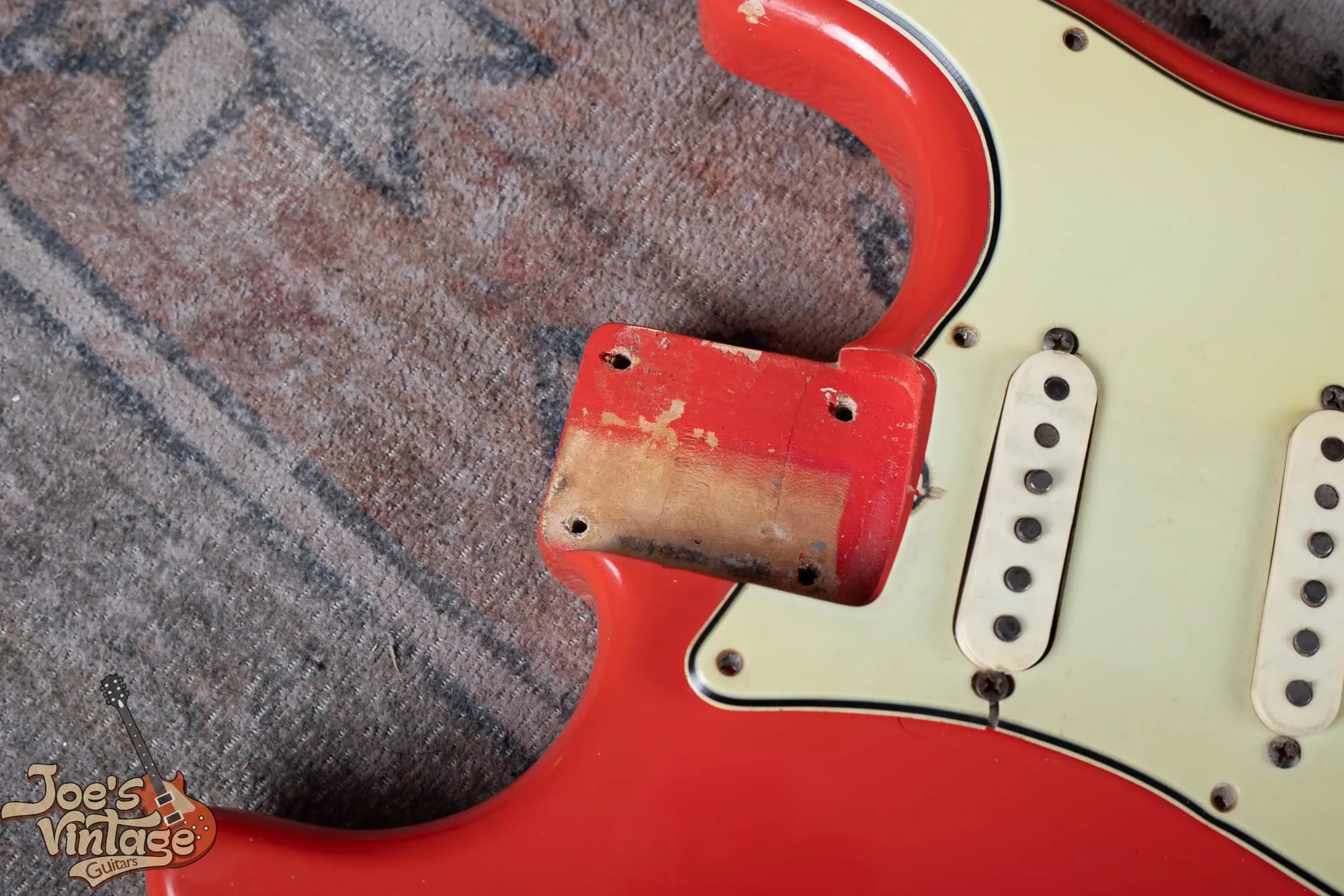 Neck pocket of a 1964 Fender Stratocaster in Fiesta Red with the neck removed, showing red color stopping at the pocket edges and bare pale wood across most of the pocket floor with no yellow sealer, next to the mint green pickguard.