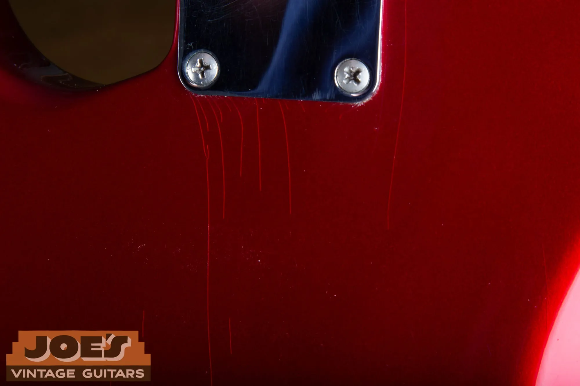 Extreme close-up of Candy Apple Red finish beside the neck plate of a 1965 Fender Stratocaster, showing fine vertical lacquer checking.