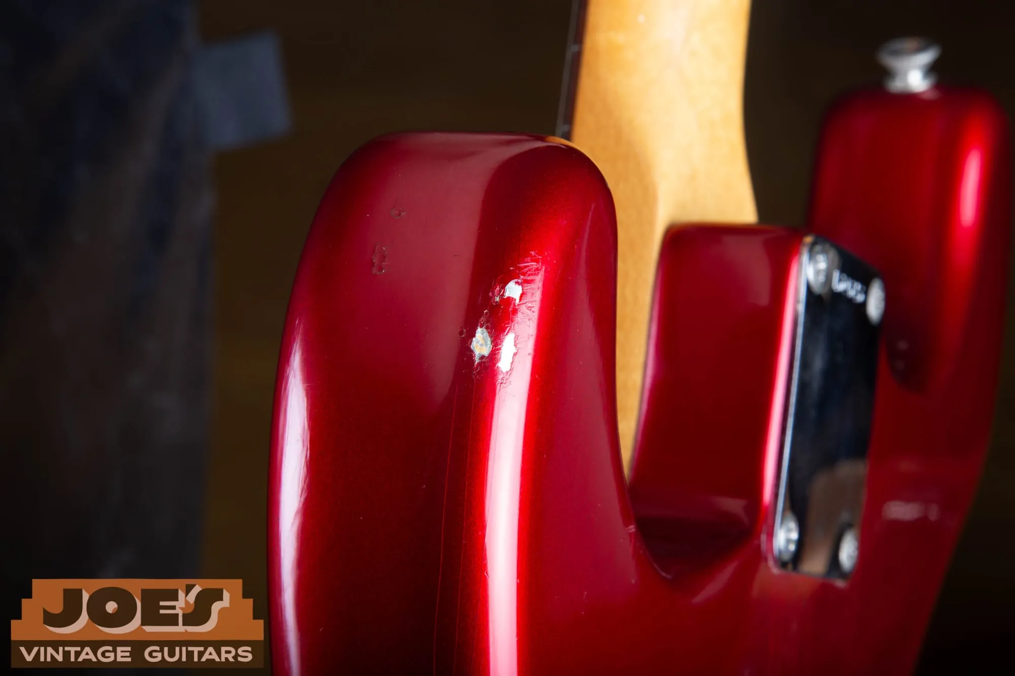 Close-up of chips on the back of the upper horn of a 1965 Fender Stratocaster in Candy Apple Red, with small chips in the red revealing a bright silver metallic undercoat beneath.