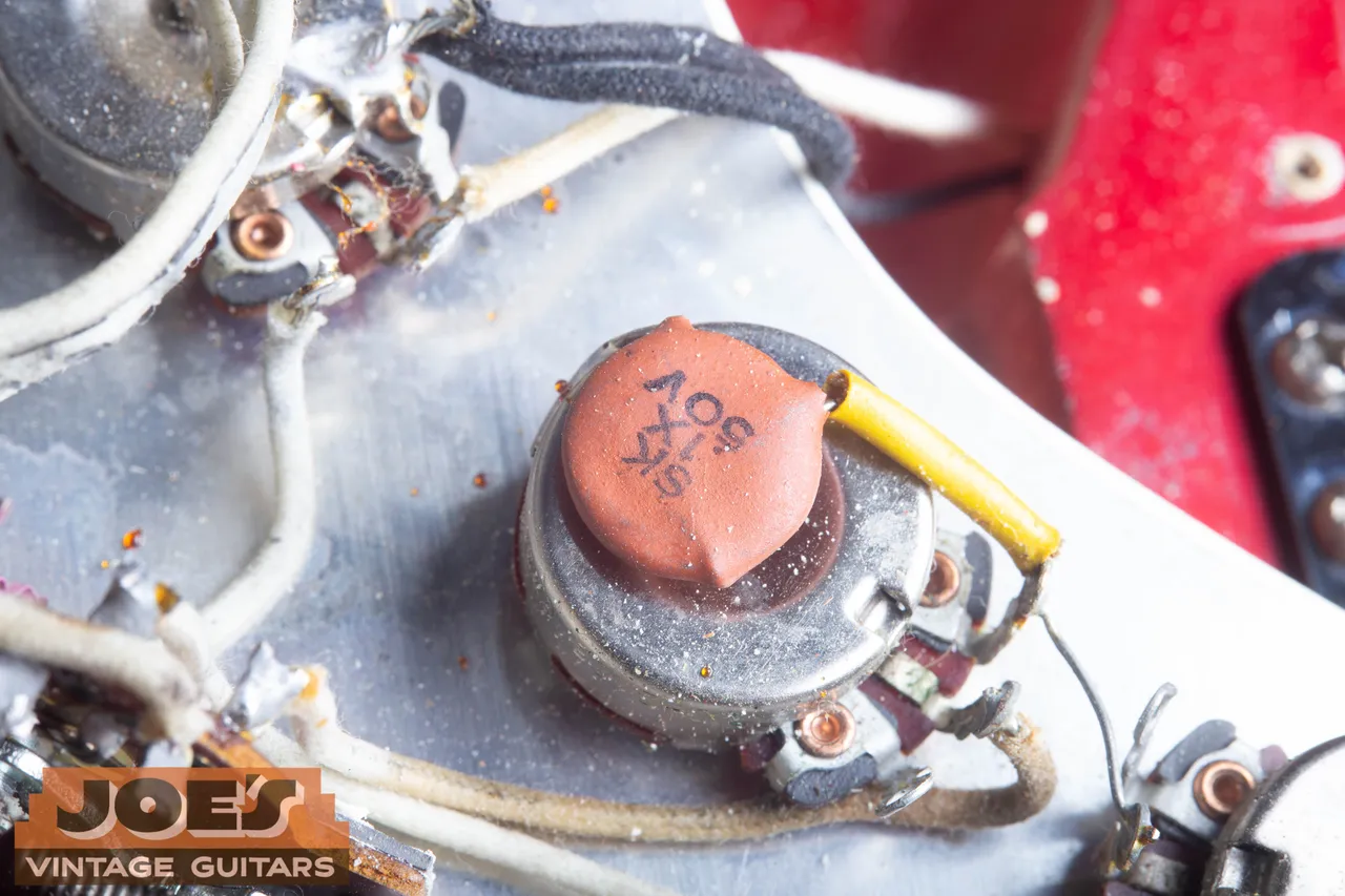 The orange ceramic disc capacitor in a 1965 Fender Stratocaster, marked .1X 50V, sitting on top of the tone pot