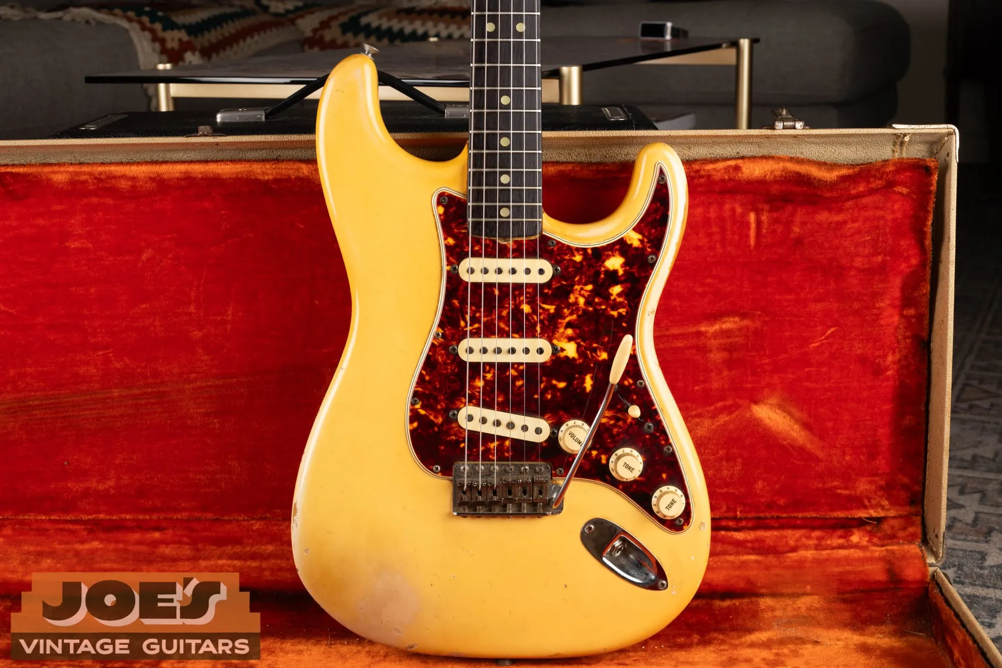 A 1965 Fender Stratocaster in Olympic White, aged to a warm cream, with a tortoiseshell pickguard, in its original case with orange lining.