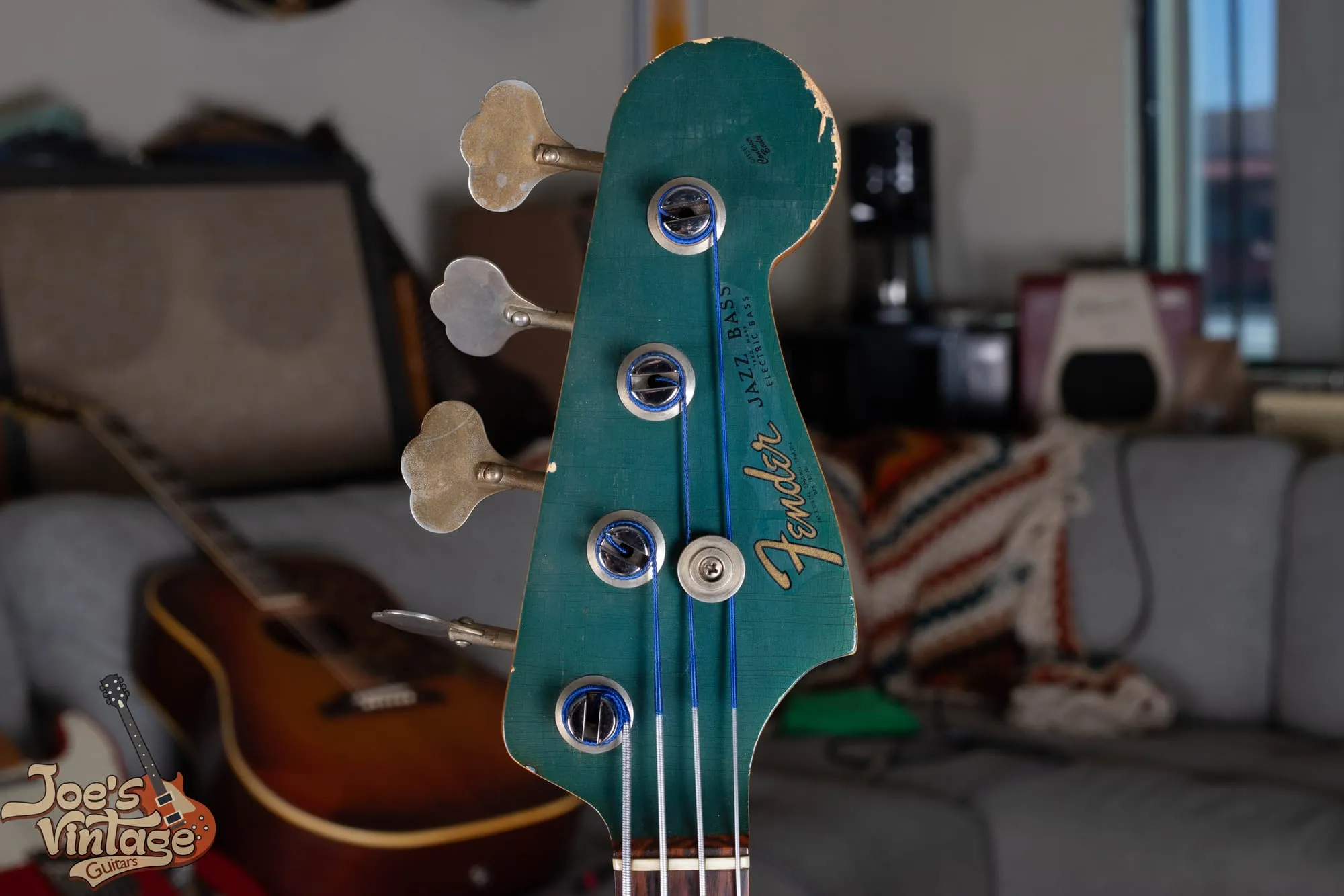 The matching painted headstock of a 1966 Fender Jazz Bass in Lake Placid Blue that has aged toward teal green, showing the gold transition logo, heavy lacquer checking, and edge wear through to the wood.