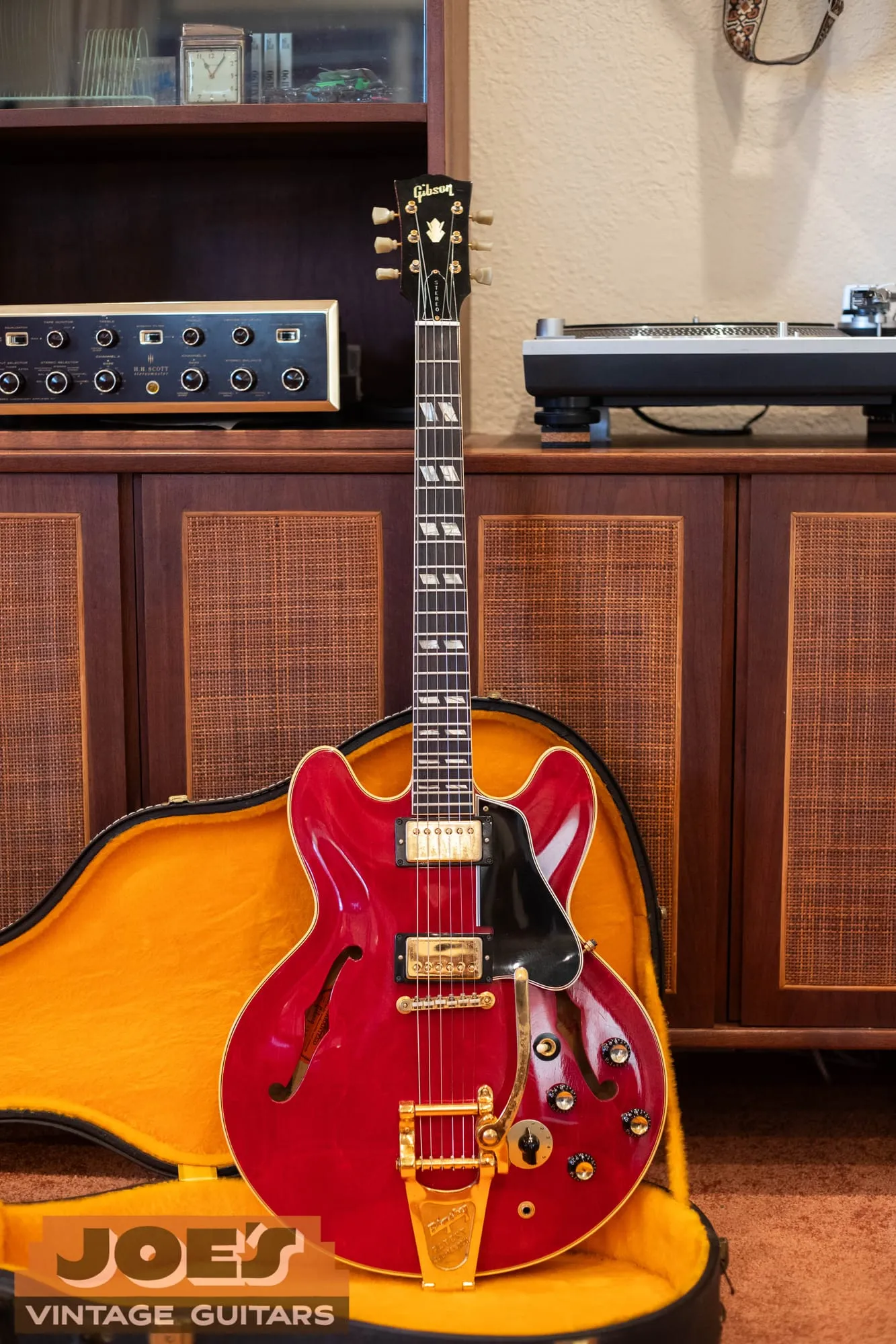 A 1966 Gibson ES-345TDC in cherry red with gold hardware and a gold Bigsby, photographed standing in front of vintage stereo equipment.