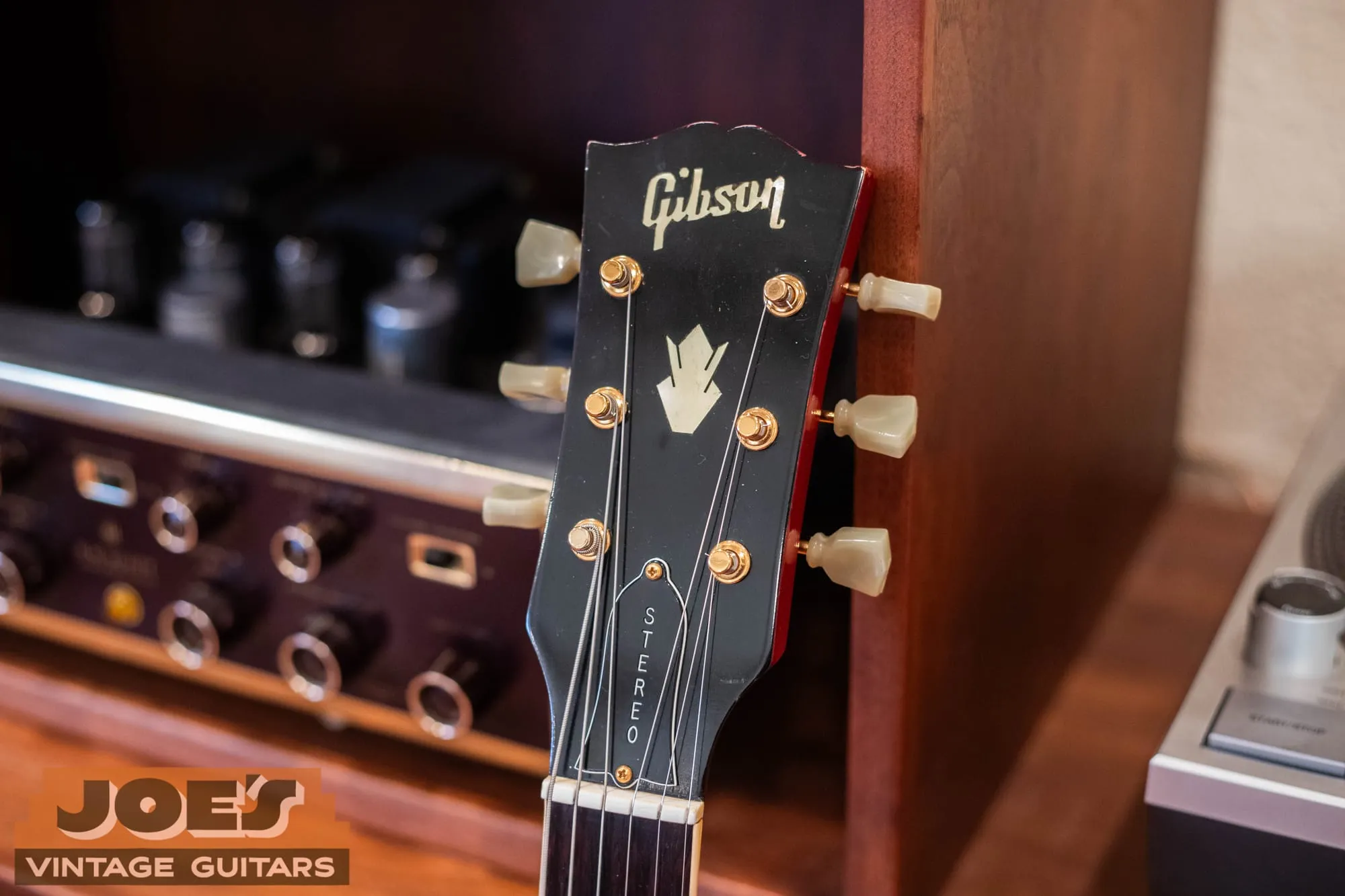 The headstock of a 1966 Gibson ES-345 with the pearl crown inlay and STEREO truss-rod cover, resting against vintage stereo equipment.