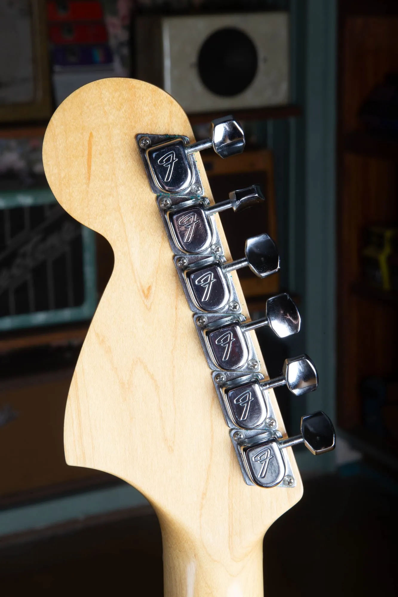 Back of a 1967 Fender Stratocaster headstock showing six Fender F stamped tuners, each with a large stylized F on the chrome cover and an octagonal metal button, on a natural maple headstock.