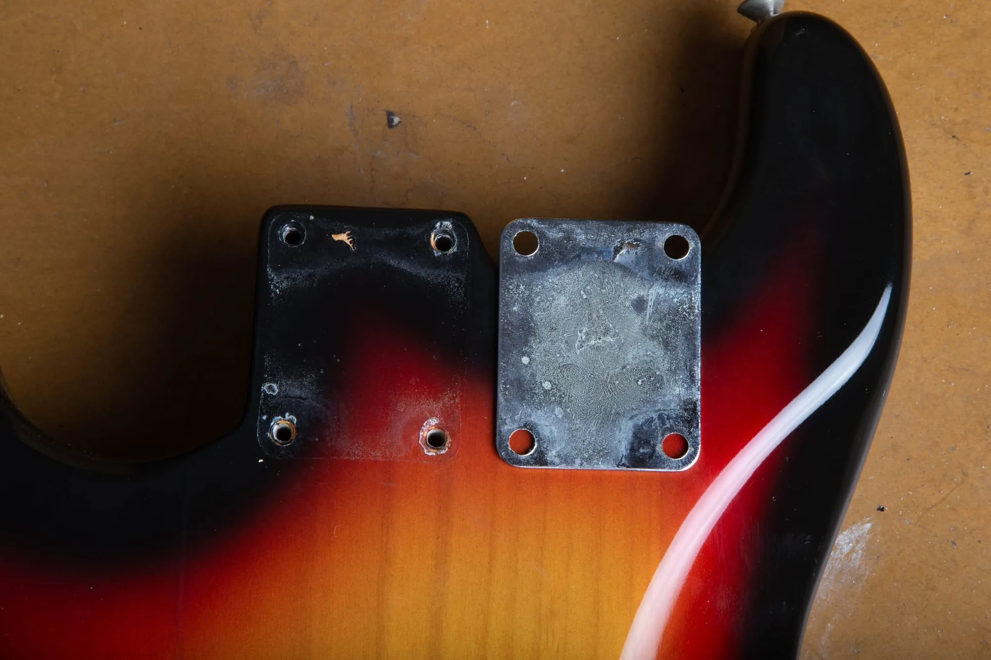 1967 Fender Stratocaster with the neck plate removed, showing the four empty screw holes in the sunburst body next to the patinated back of the chrome F plate.