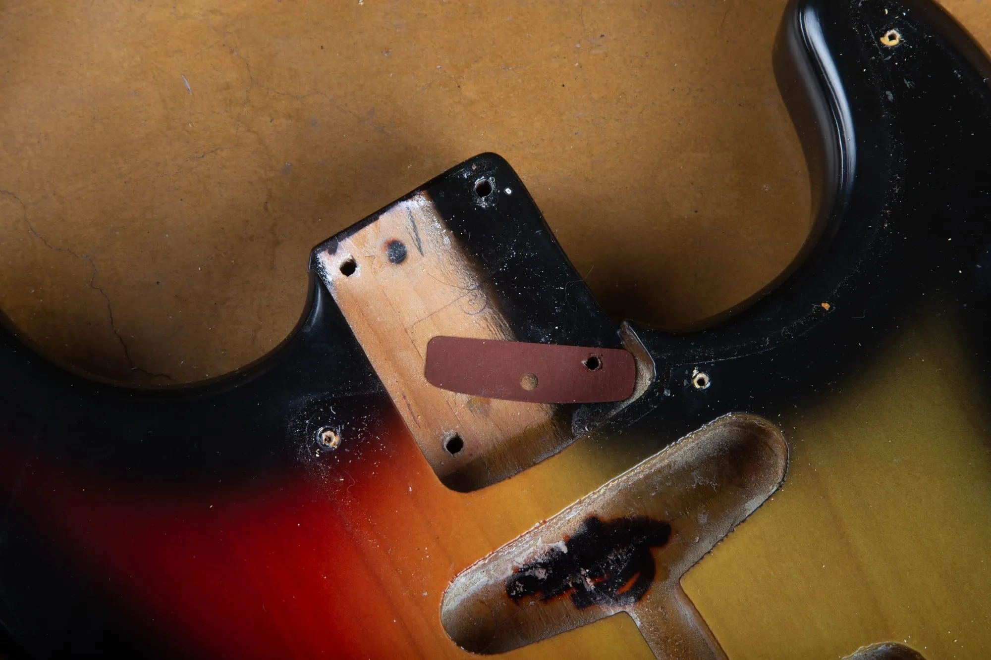 Neck pocket of a 1967 Fender Stratocaster with the neck removed, showing the dark red vulcanized fiber shim, bare-wood paint stick area, and heavy finish checking around the pocket.