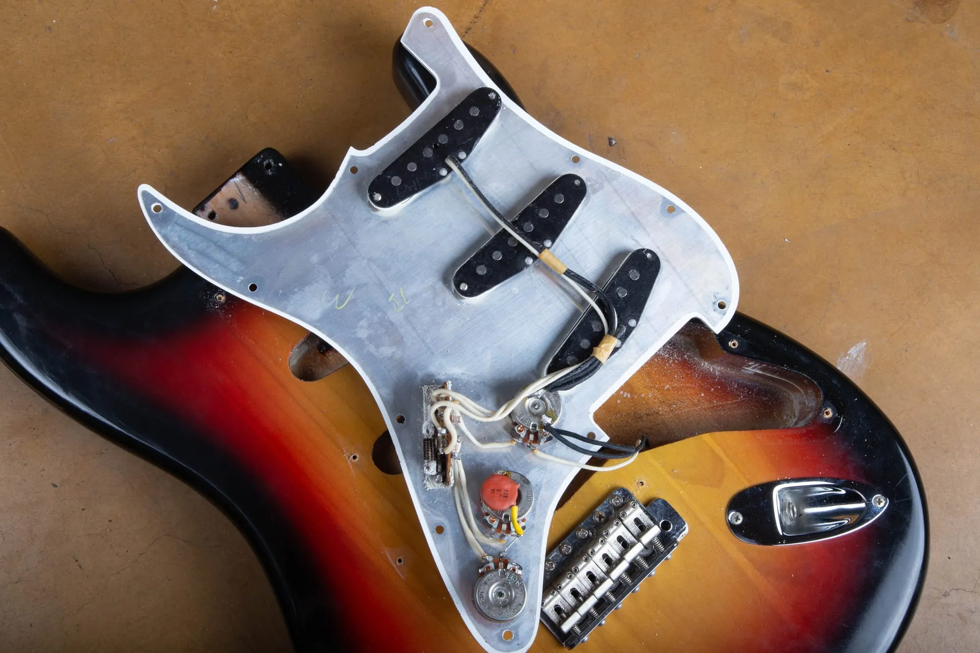 Wiring harness of a 1967 Fender Stratocaster lifted out on the pickguard, showing three staggered single-coil pickups, cloth-covered pushback wire, a ceramic disc capacitor, three potentiometers, and the three-way selector switch, with the body routes visible below.
