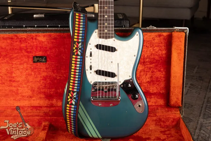 Front of a 1971 Fender Competition Mustang in Competition Blue with seafoam racing stripes, a pearloid pickguard, and the Dynamic Vibrato, in its original orange-lined case. We buy vintage Fender Mustangs nationwide at Joe's Vintage Guitars.