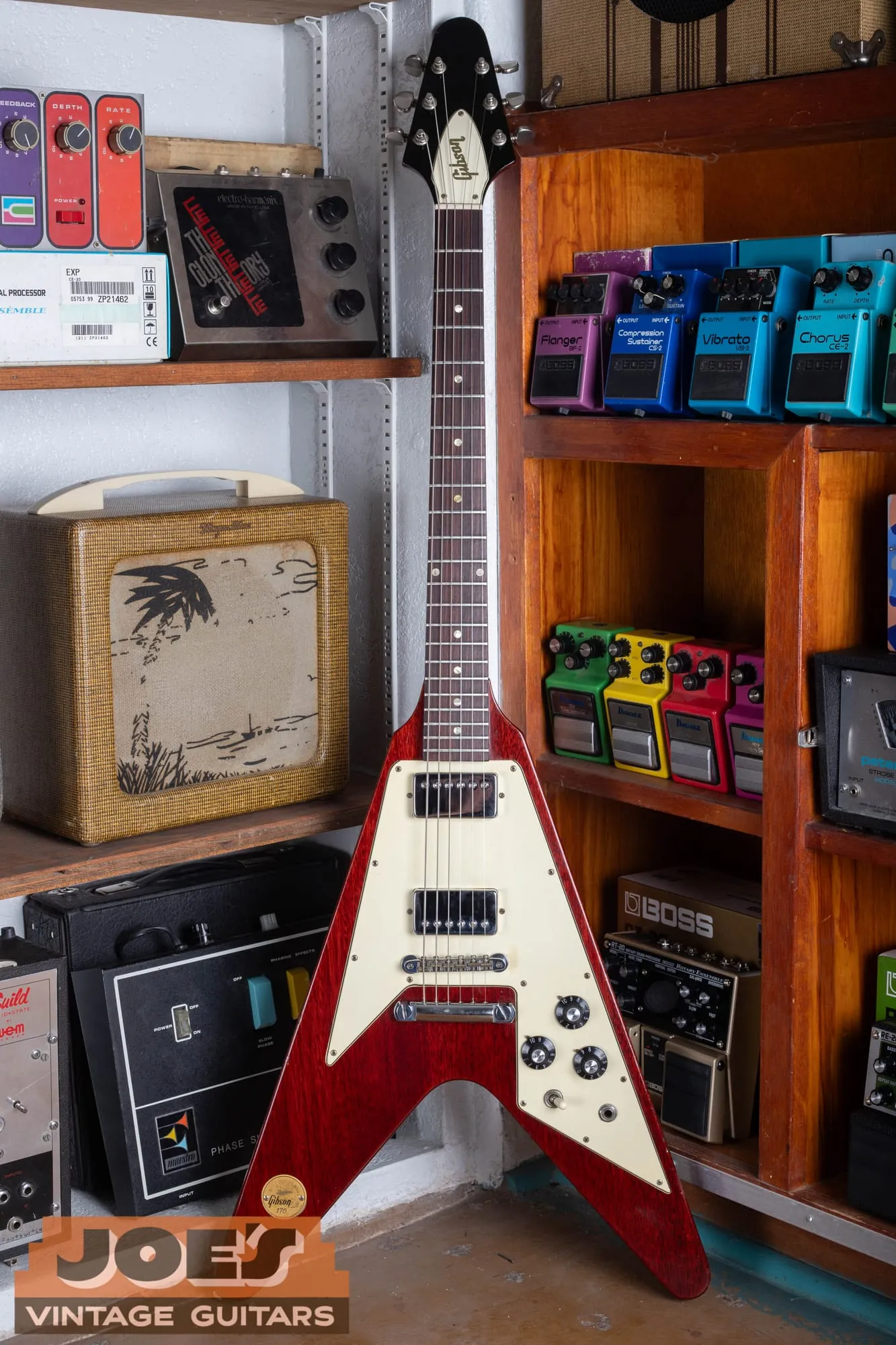Full front of a 1971 Gibson Flying V Medallion in cherry, standing upright, with the large cream three-ply pickguard, two chrome-covered humbuckers, a Tune-o-Matic bridge and stop-bar tailpiece, and the numbered gold medallion in the lower bass wing.