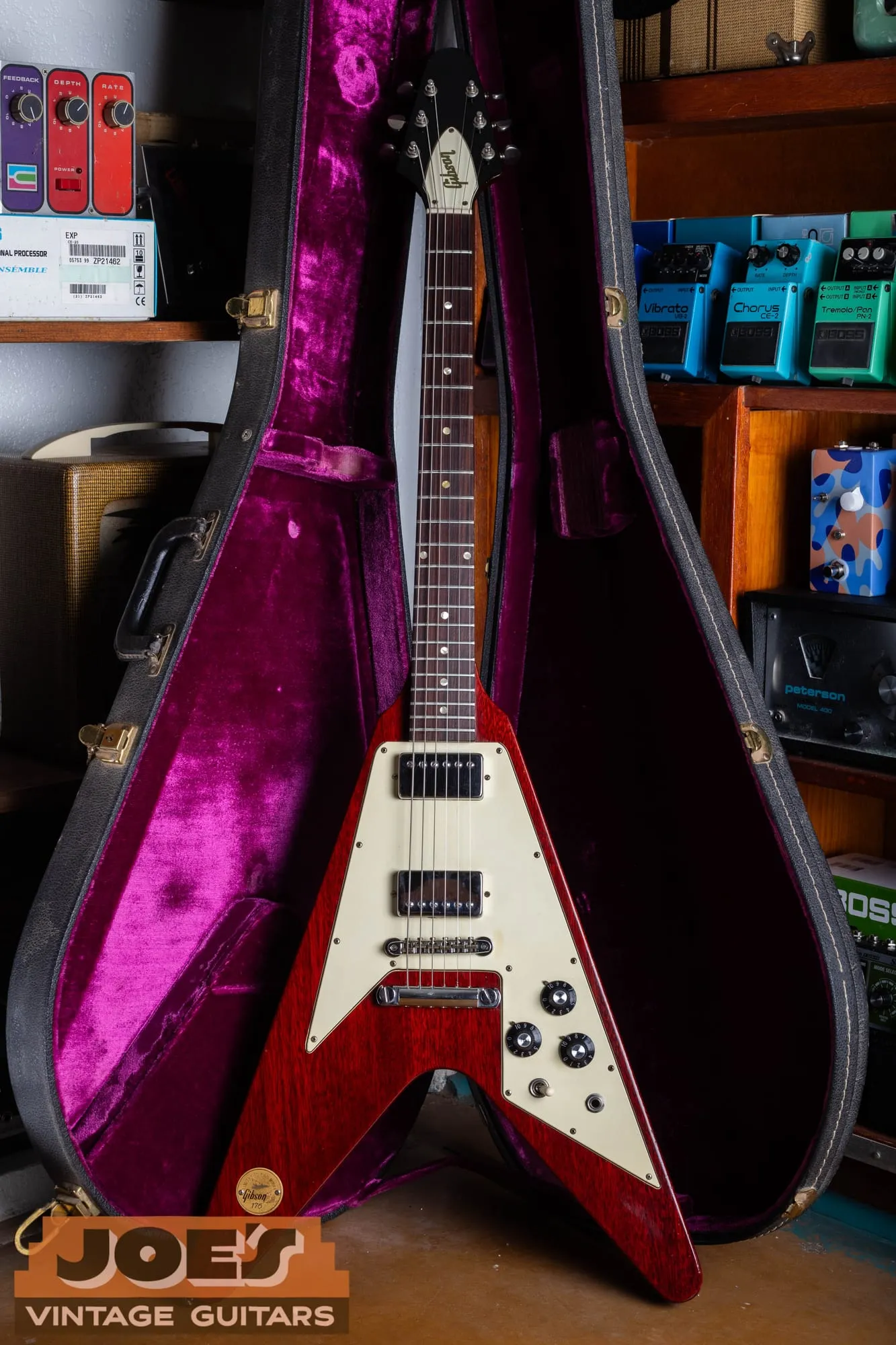 A 1971 Gibson Flying V Medallion in cherry lying in its hardshell case with a bright magenta plush lining, seen from the front.