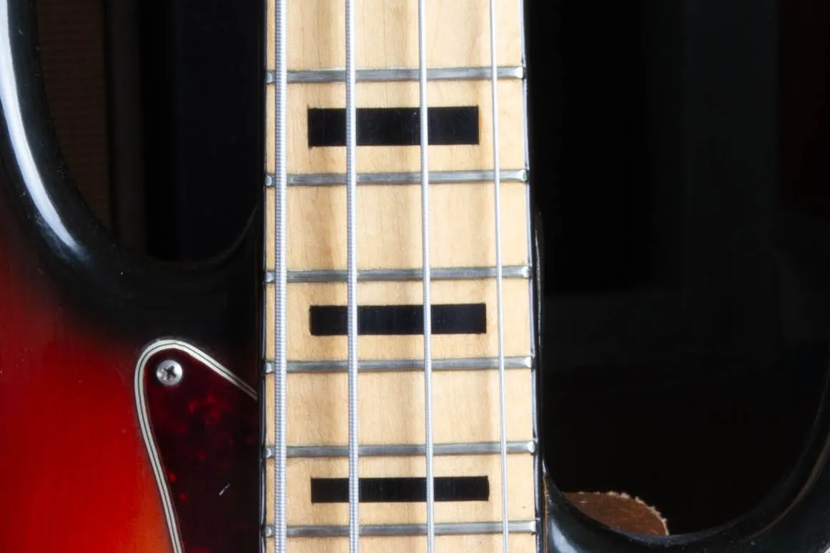 Close up of the maple fingerboard on a 1973 Fender Jazz Bass showing bold black block inlays and amber toned maple under the lacquer.