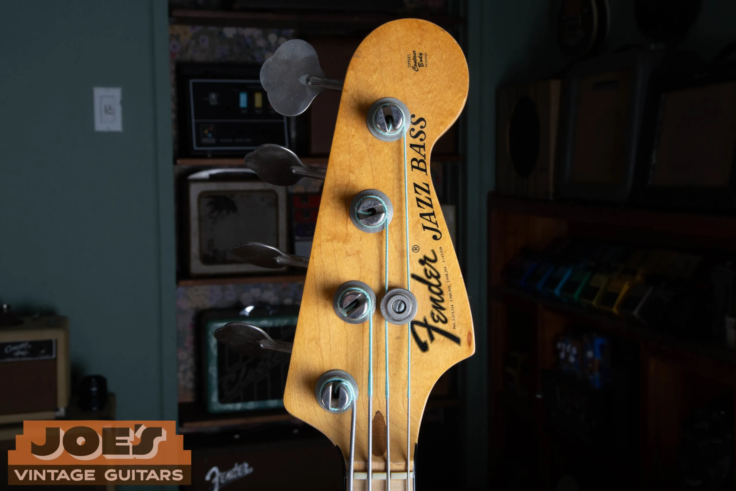 The front of the headstock on a 1973 Fender Jazz Bass showing the thick black CBS logo reading Fender Jazz Bass with the maple neck and four in line tuners.