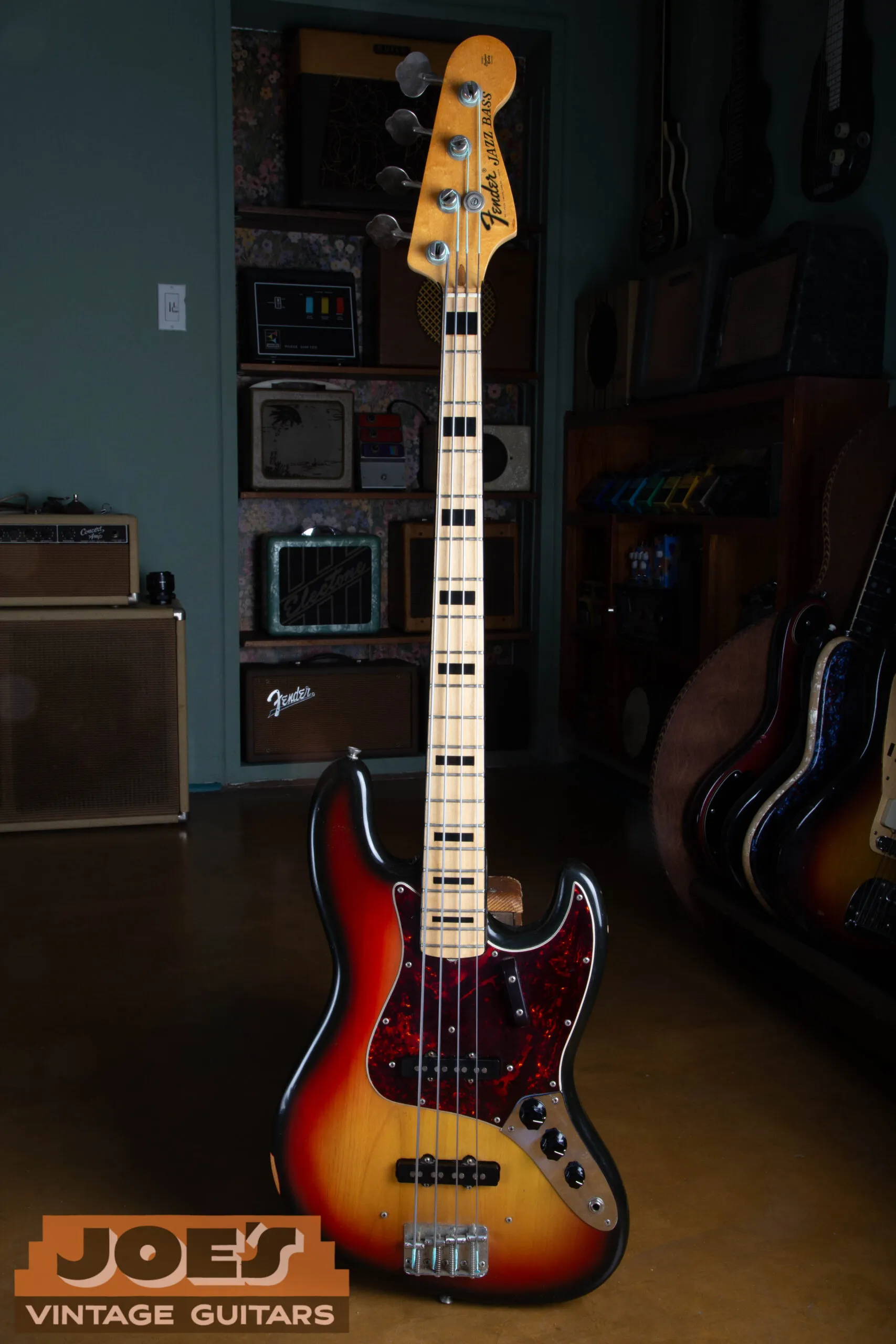 Full front view of a 1973 Fender Jazz Bass in sunburst with a maple neck, black block inlays, and a black pickguard.