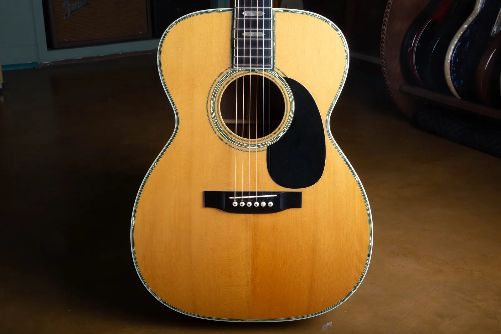 Spruce top of a 1976 Martin 000-45 showing the abalone pearl border running around the entire top edge, the abalone rosette, a black pickguard, and an ebony belly bridge with white pearl-dot pins.