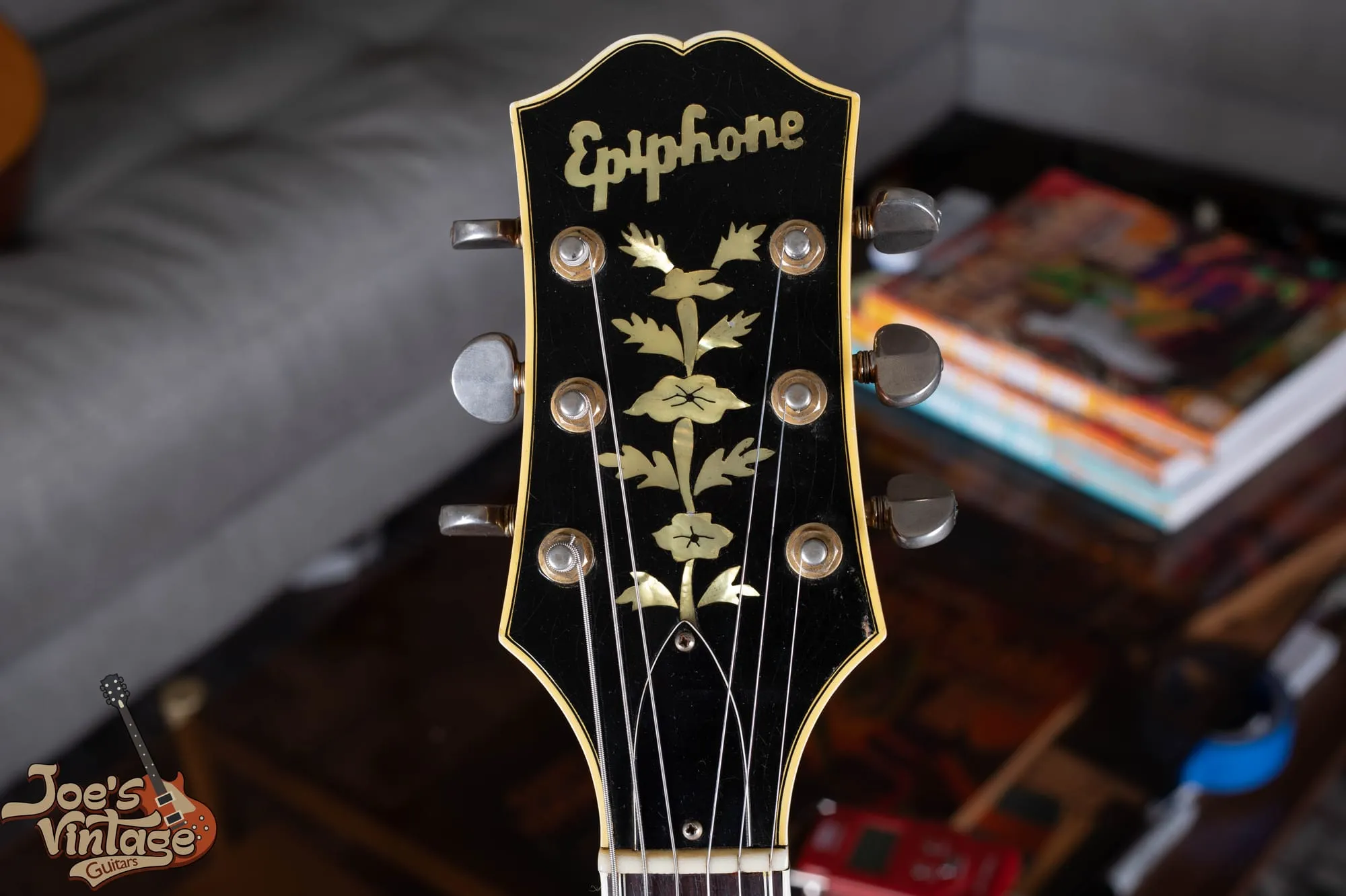 Headstock of a vintage Epiphone Sheraton showing the pearl Epiphone script logo and the flowering-vine tree of life inlay on a bound black headstock.