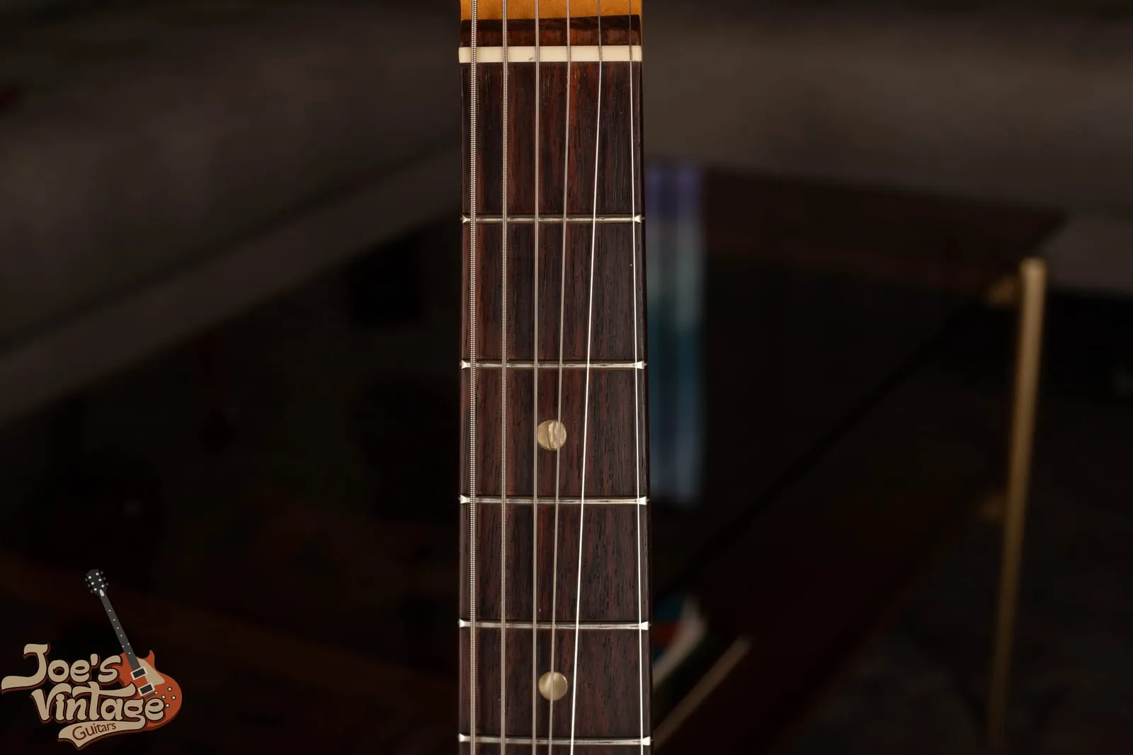 Rosewood fingerboard of a vintage Fender Mustang showing pearloid dot inlays and a bolt-on maple neck.