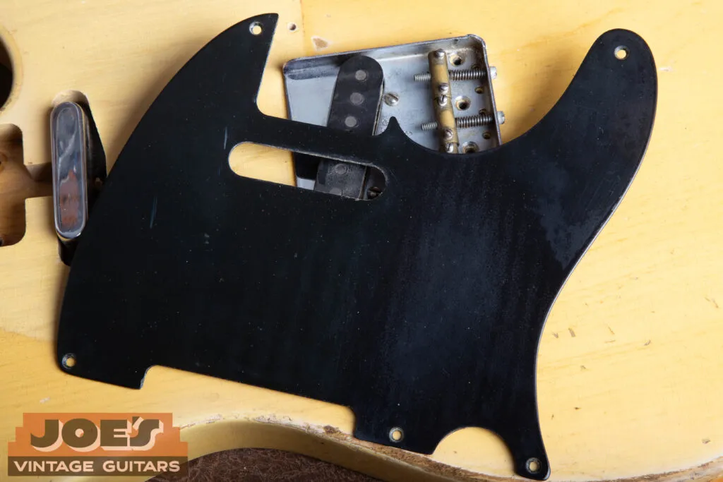 The single-ply black phenolic pickguard on a 1952 Fender Telecaster, thick and hard with no layers visible at the edge