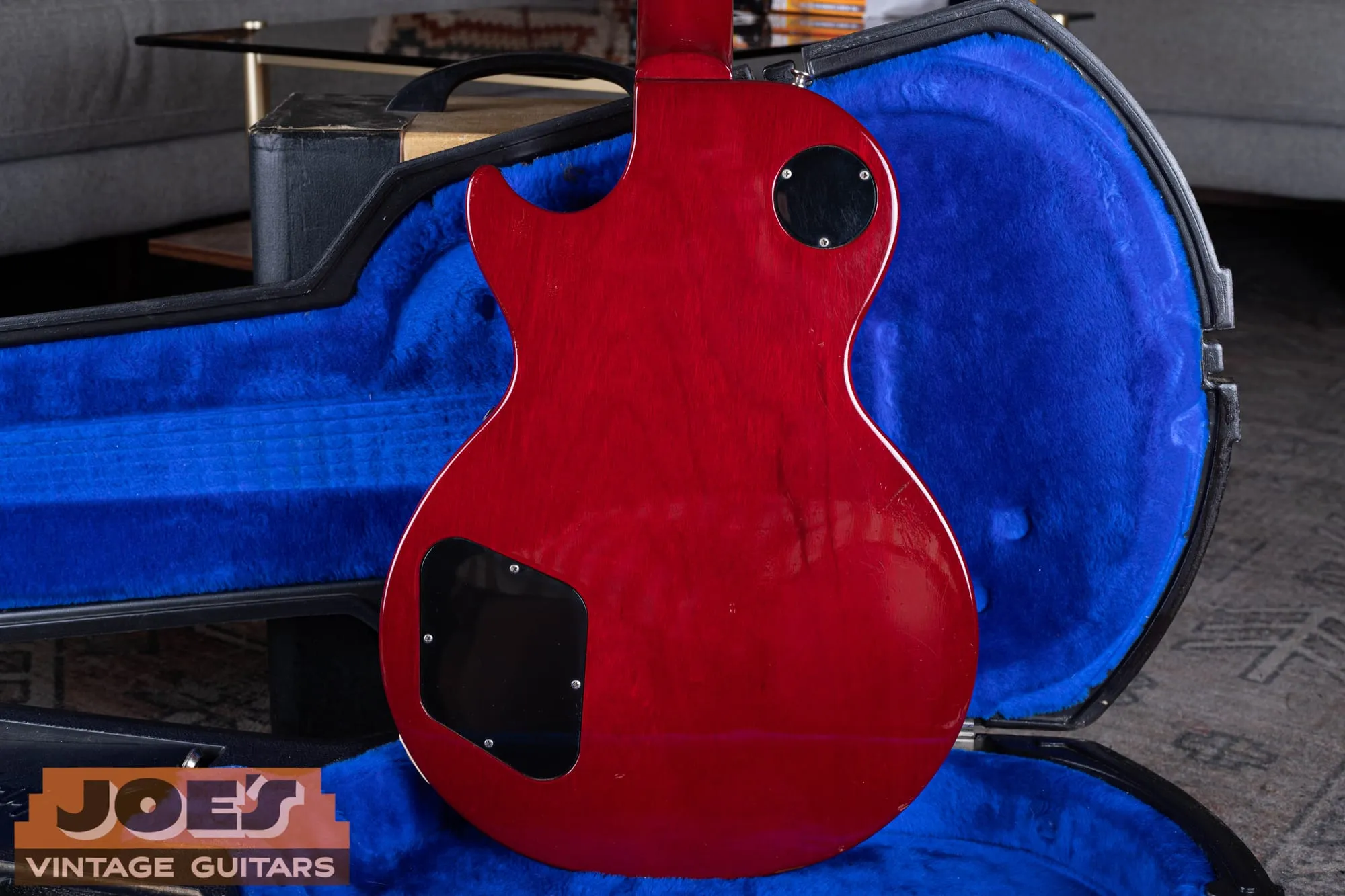 Back of a 1984 Gibson Aldo Nova Les Paul XPL showing the translucent cherry mahogany body, black control cavity cover, and switch cavity cover, lying in a blue-lined hardshell case.