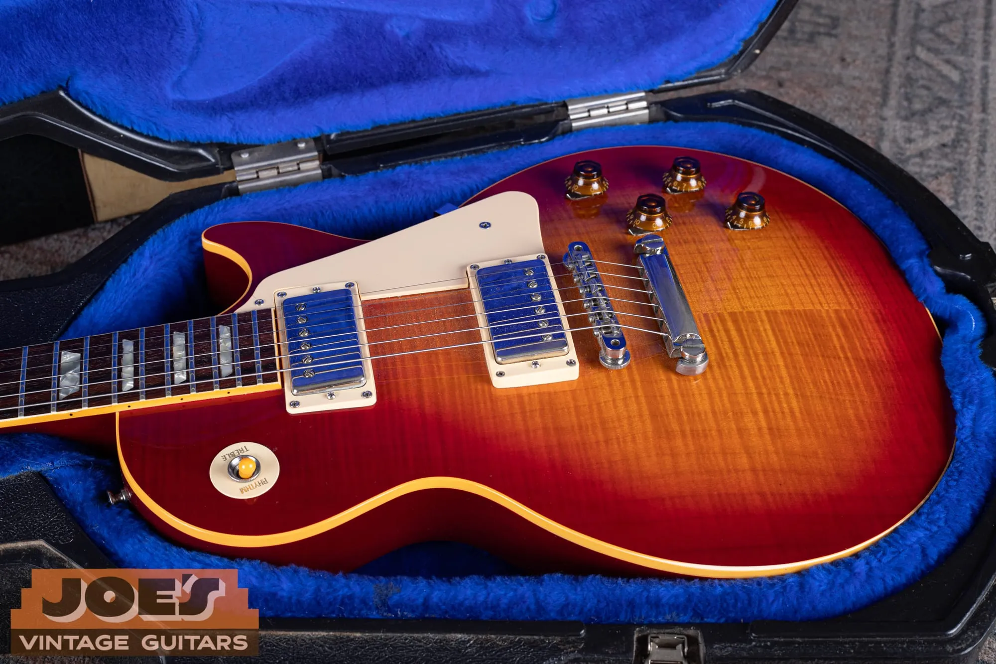 Upper body of a 1984 Gibson Aldo Nova Les Paul XPL showing two chrome humbuckers with cream rings, cream pickguard, amber top-hat knobs, and a Tune-o-Matic bridge with stopbar tailpiece over a flamed cherry sunburst top.