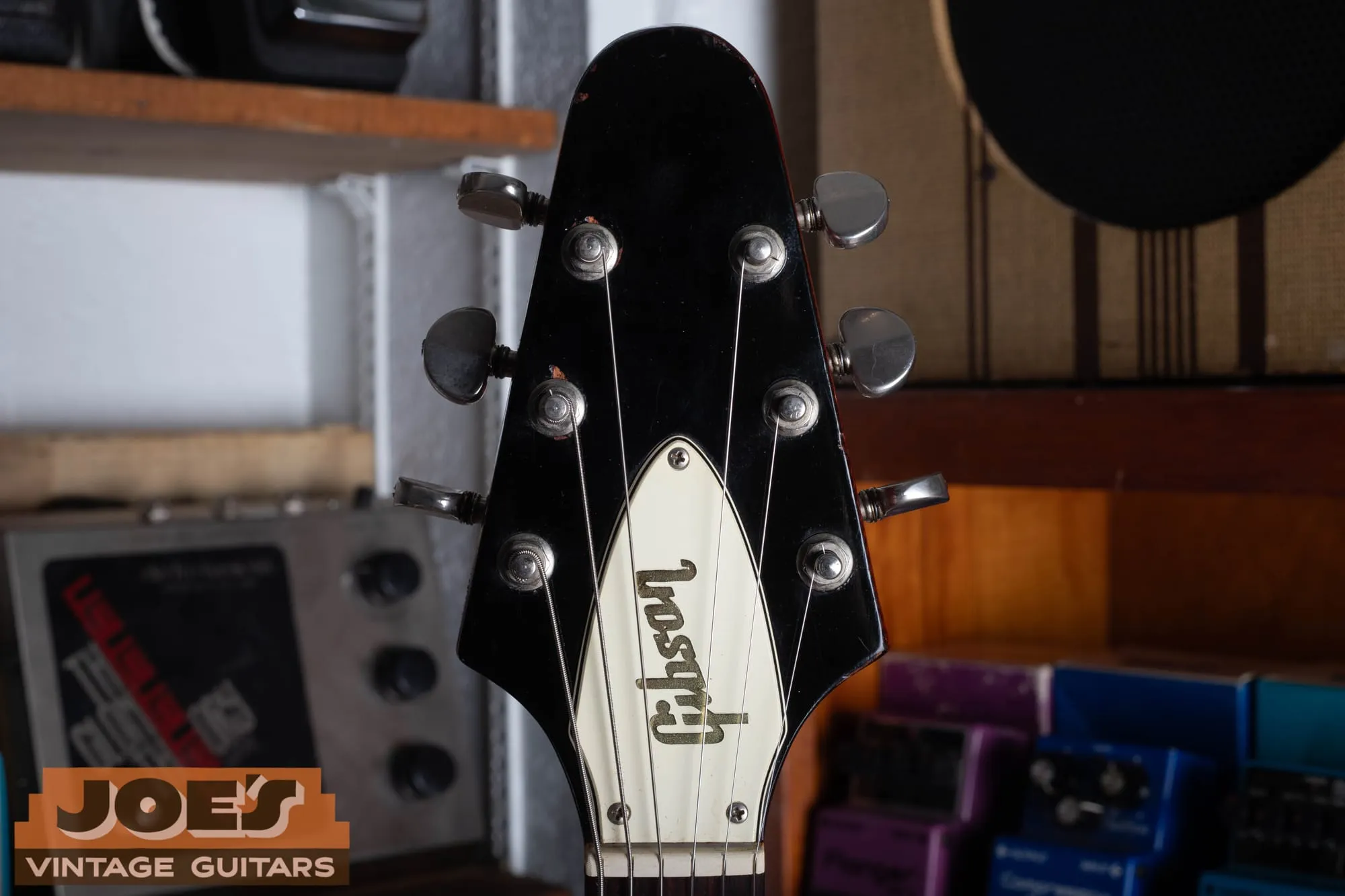 Front of the black headstock on a 1971 Gibson Flying V Medallion, with the gold Gibson script logo, a white bell-shaped truss rod cover, and three tuners per side.