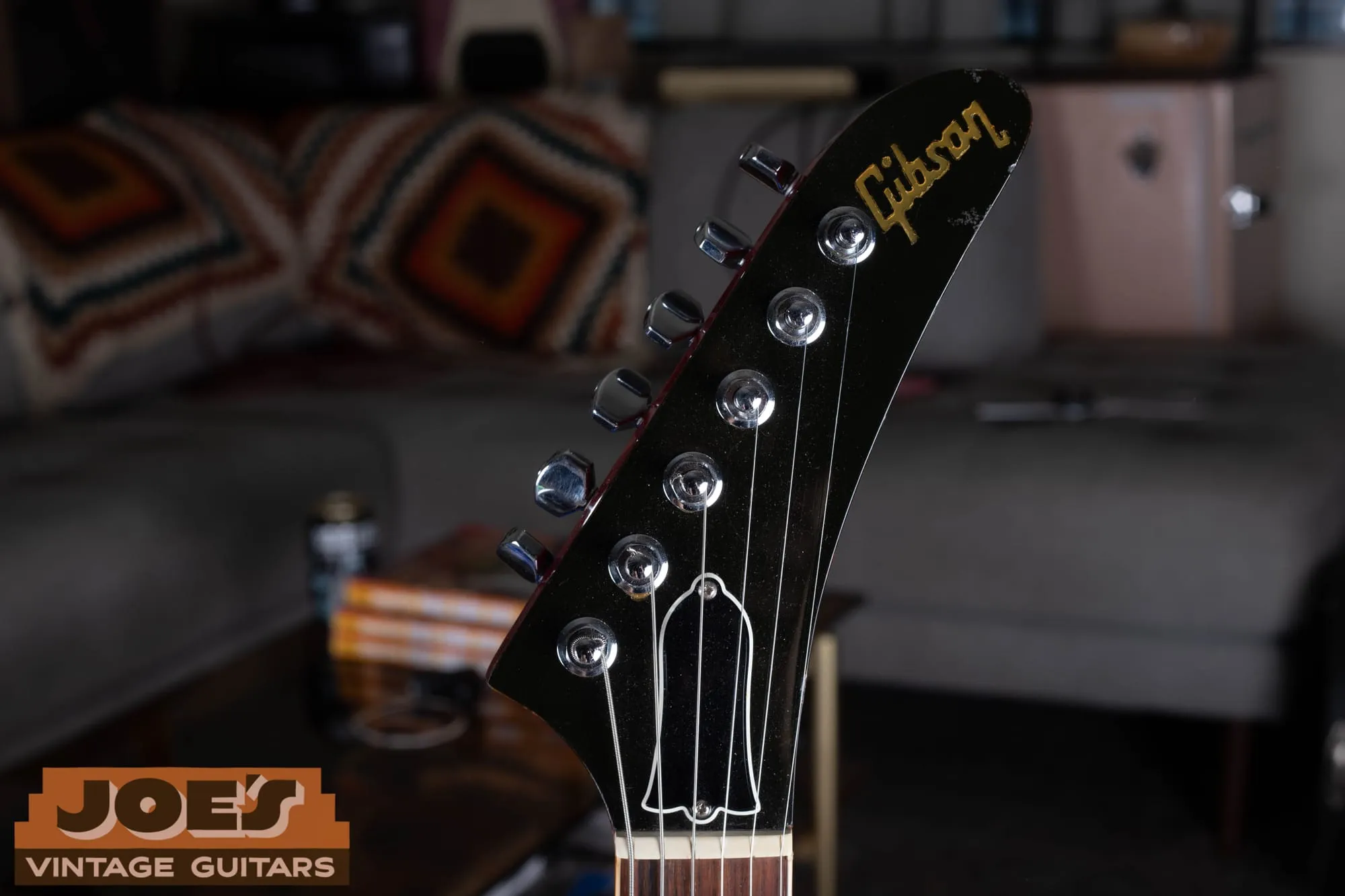 Front of the pointed Explorer-style headstock on a Gibson Les Paul XPL, with a black face, a gold Gibson logo, a blank bell-shaped truss rod cover, and six chrome tuners in a row.