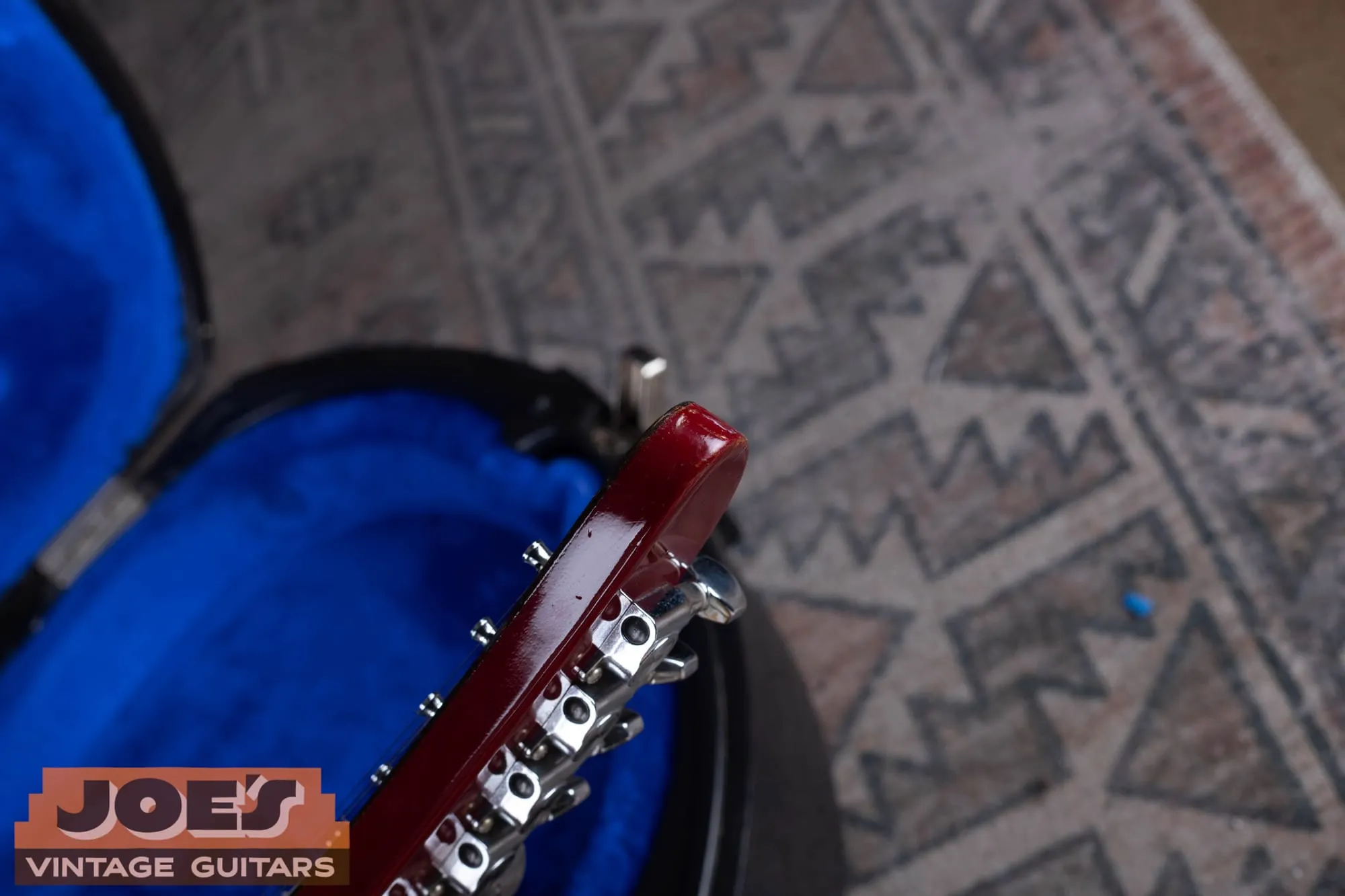 The pointed tip of a Gibson Les Paul XPL Explorer headstock in translucent cherry, resting in a blue-lined case.