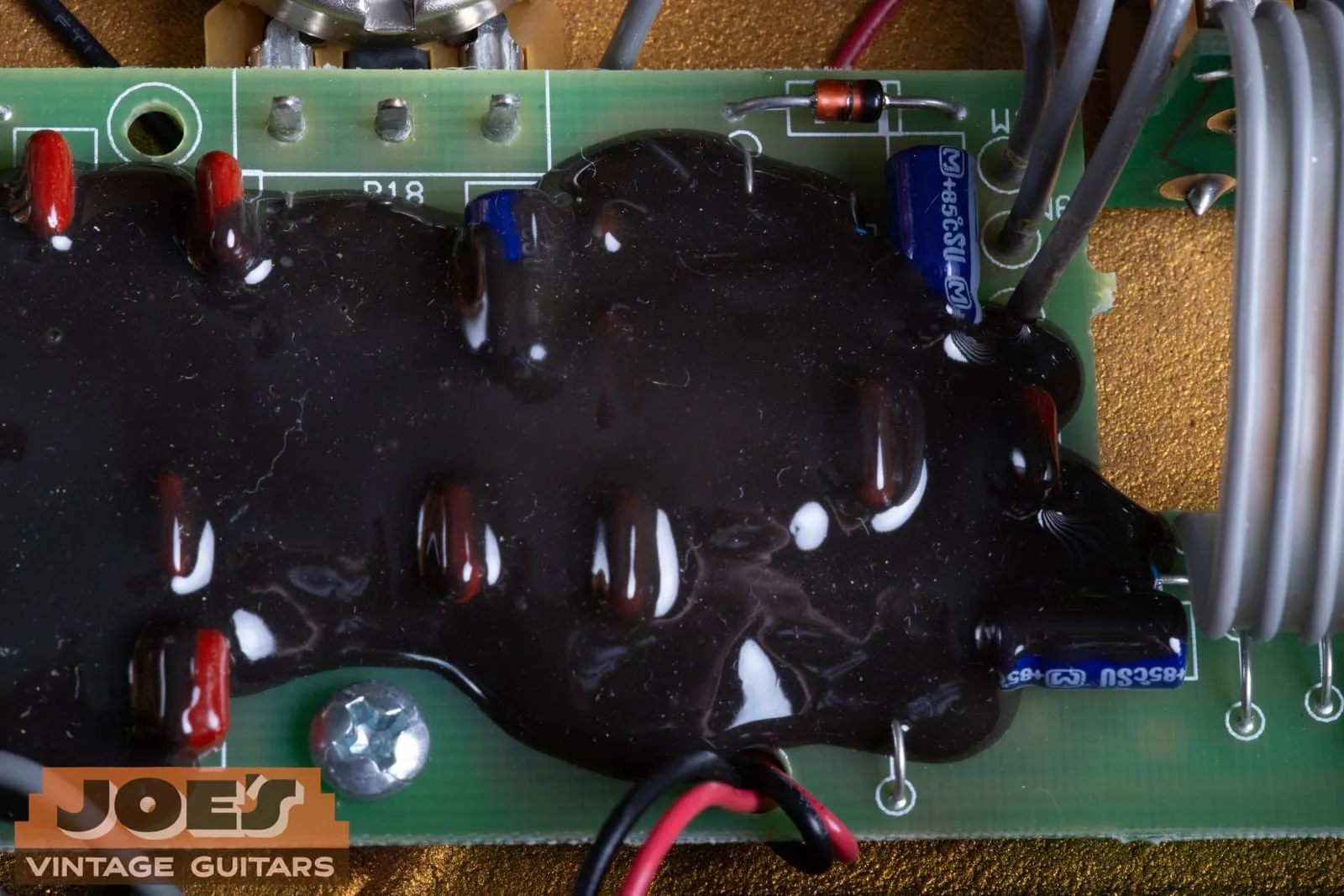 The black epoxy goop covering part of the circuit board inside a Klon Centaur, with resistor and capacitor tops visible as bumps through the glossy surface.